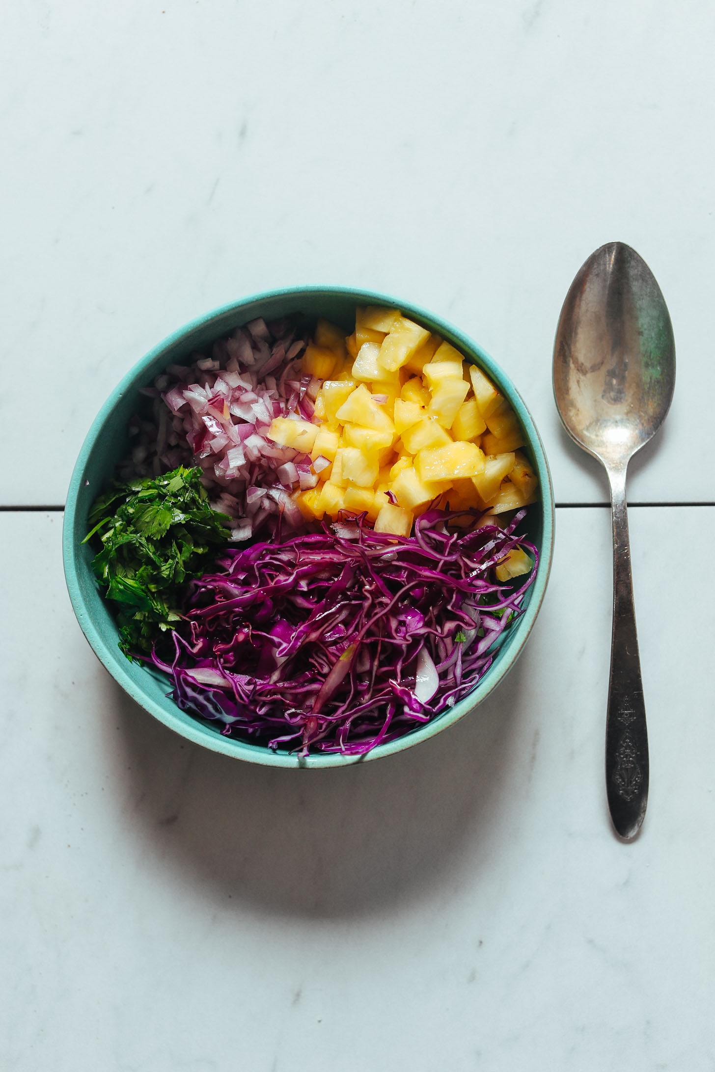 Bowl of diced pineapple, red onion, red cabbage, and cilantro ready to be stirred together for a Pineapple Cabbage Slaw