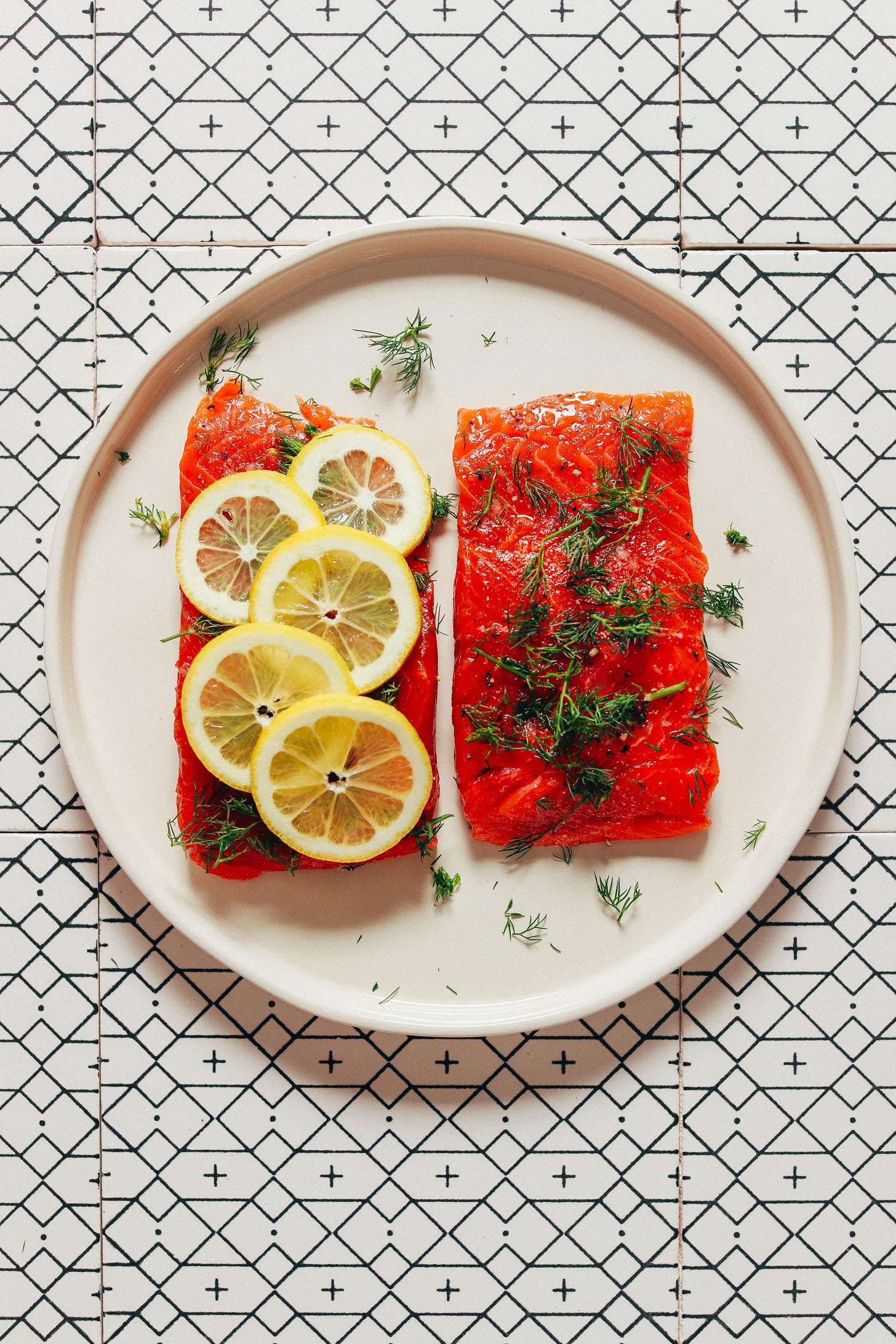 Two filets of salmon; one topped with dill and the other with lemon slices and dill