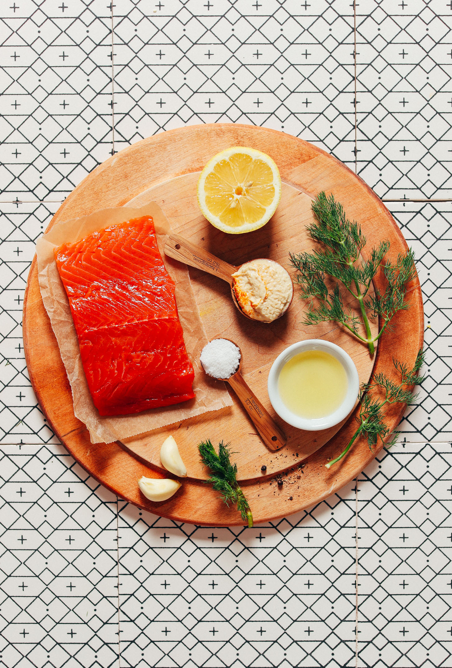 Wood cutting board with vibrant wild-caught salmon, garlic, dill, lemon, and other ingredients for making a delicious salmon recipe