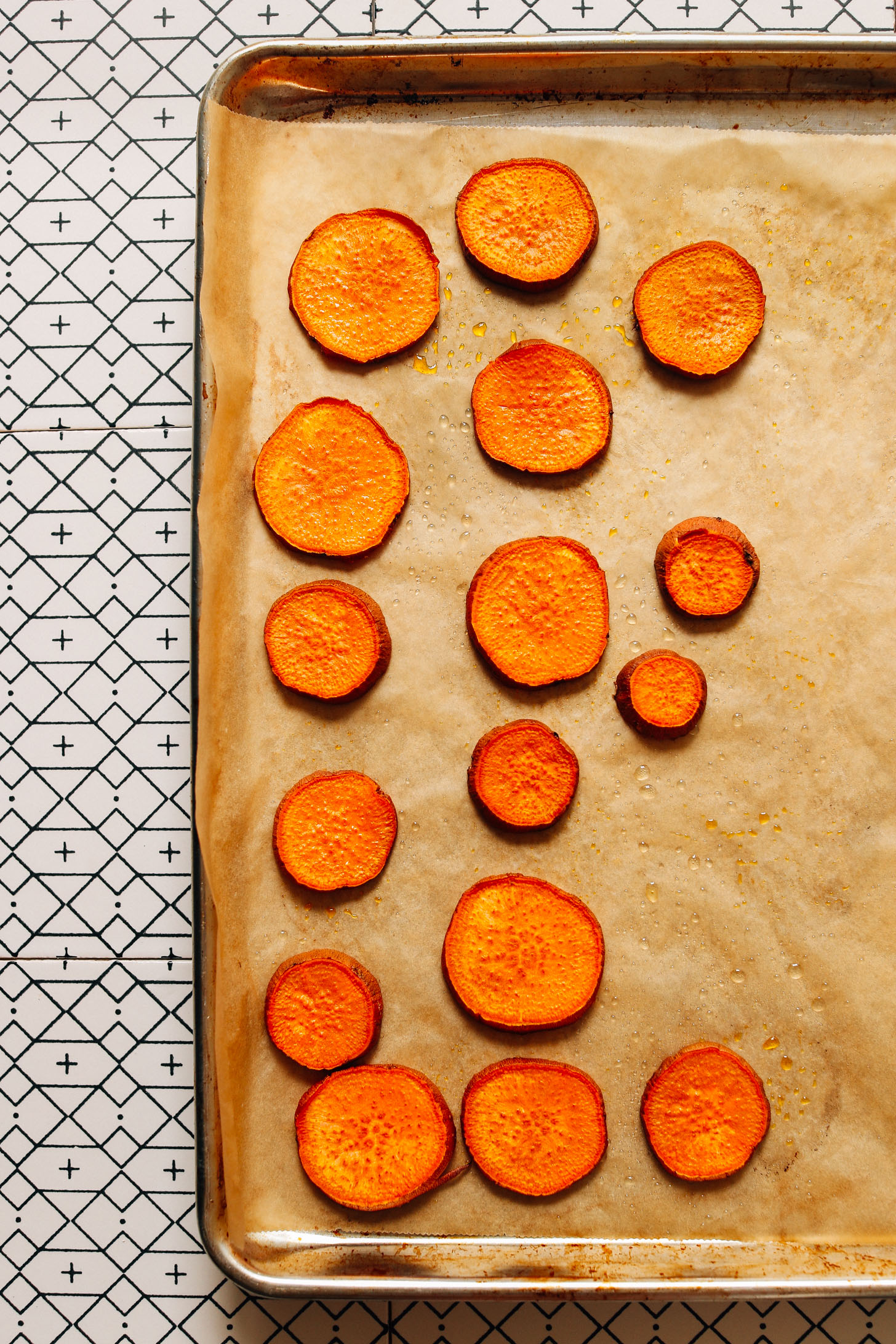 Parchment-lined baking sheet of freshly roasted sweet potato rounds for making Gado Gado