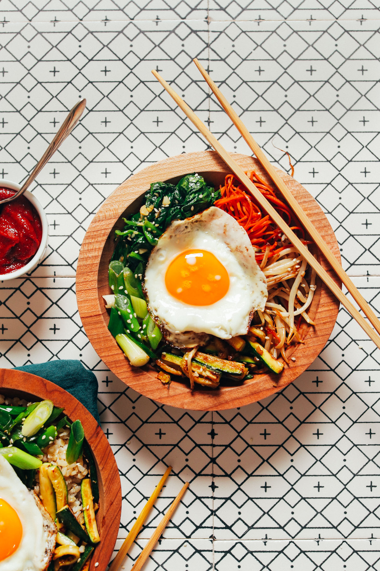 Chopsticks resting on and beside bowls of homemade Korean Bibimbap with fried eggs