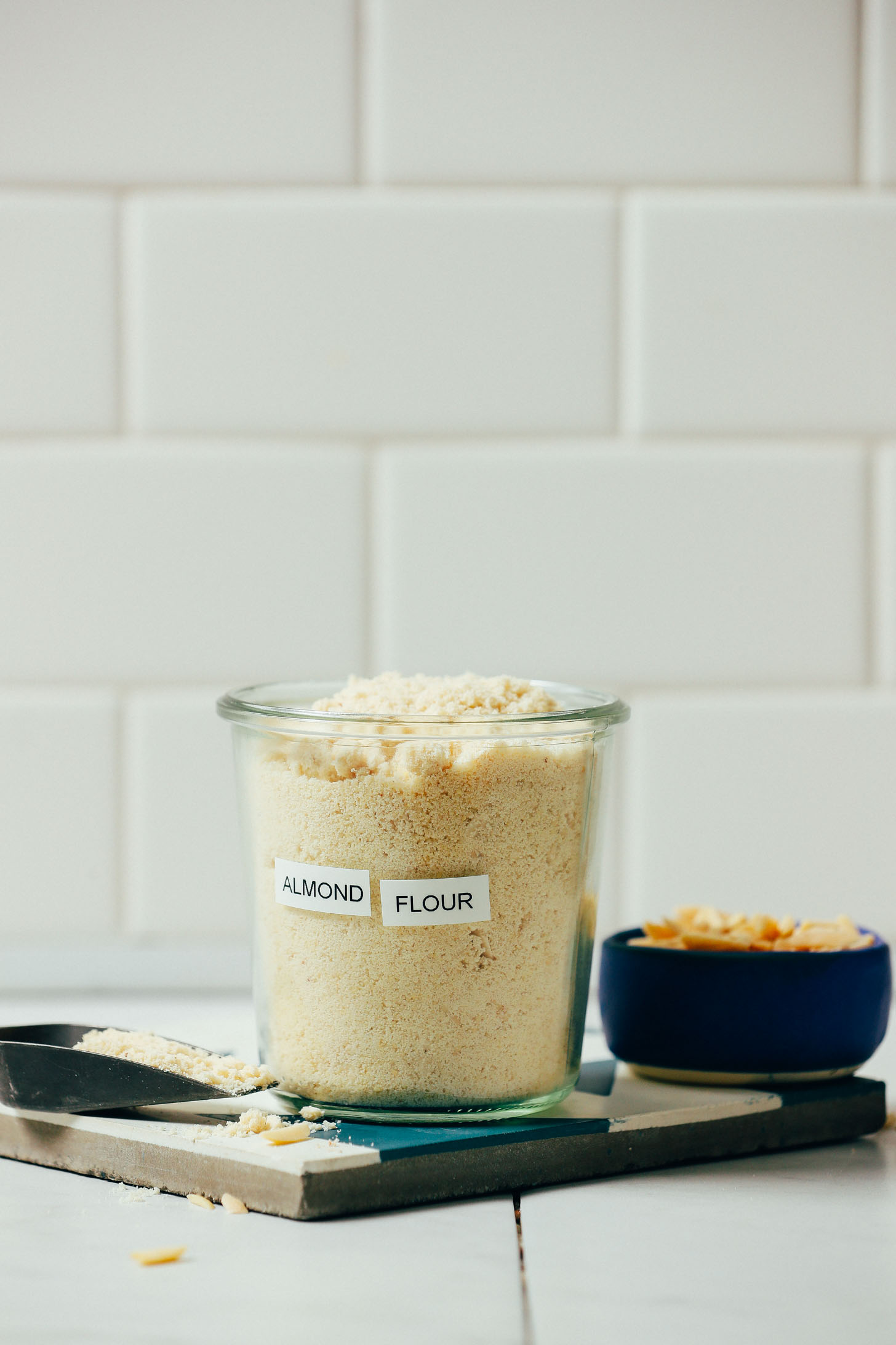 Jar of homemade almond flour beside a bowl of blanched almonds