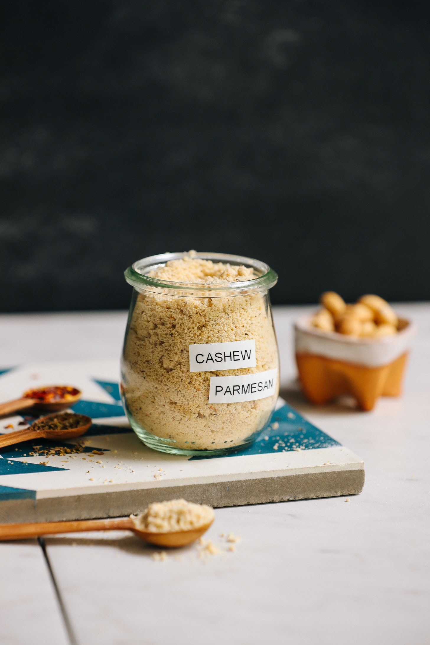 Jar of yeast-free, dairy-free, homemade Parmesan cheese beside ingredients used to make it