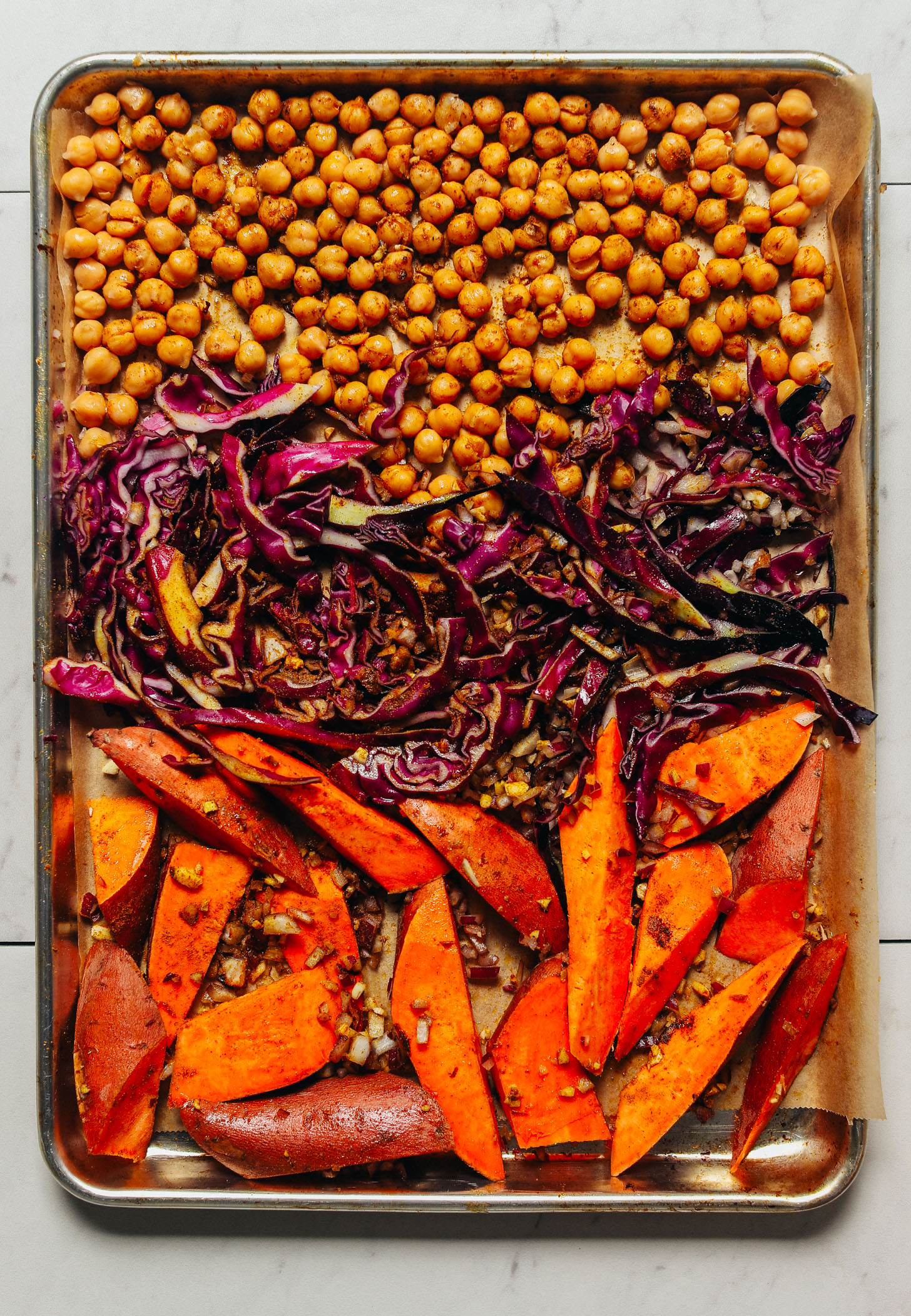 Baking sheet filled with sweet potatoes, cabbage, and chickpeas topped with curry powder