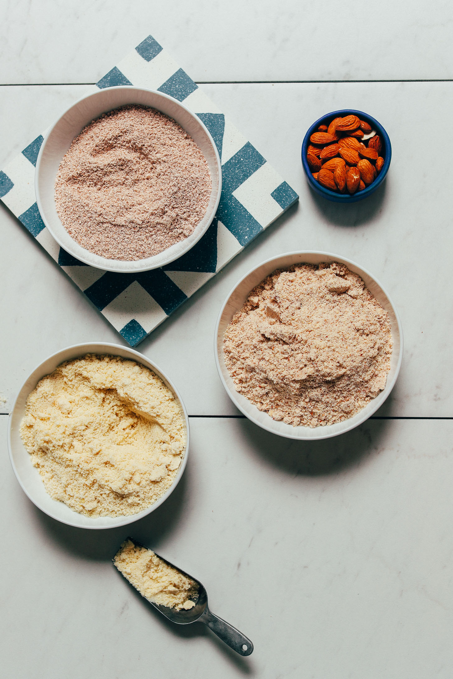 Bowls of almond flour and two different types of almond meal with one being made from leftover almond pulp