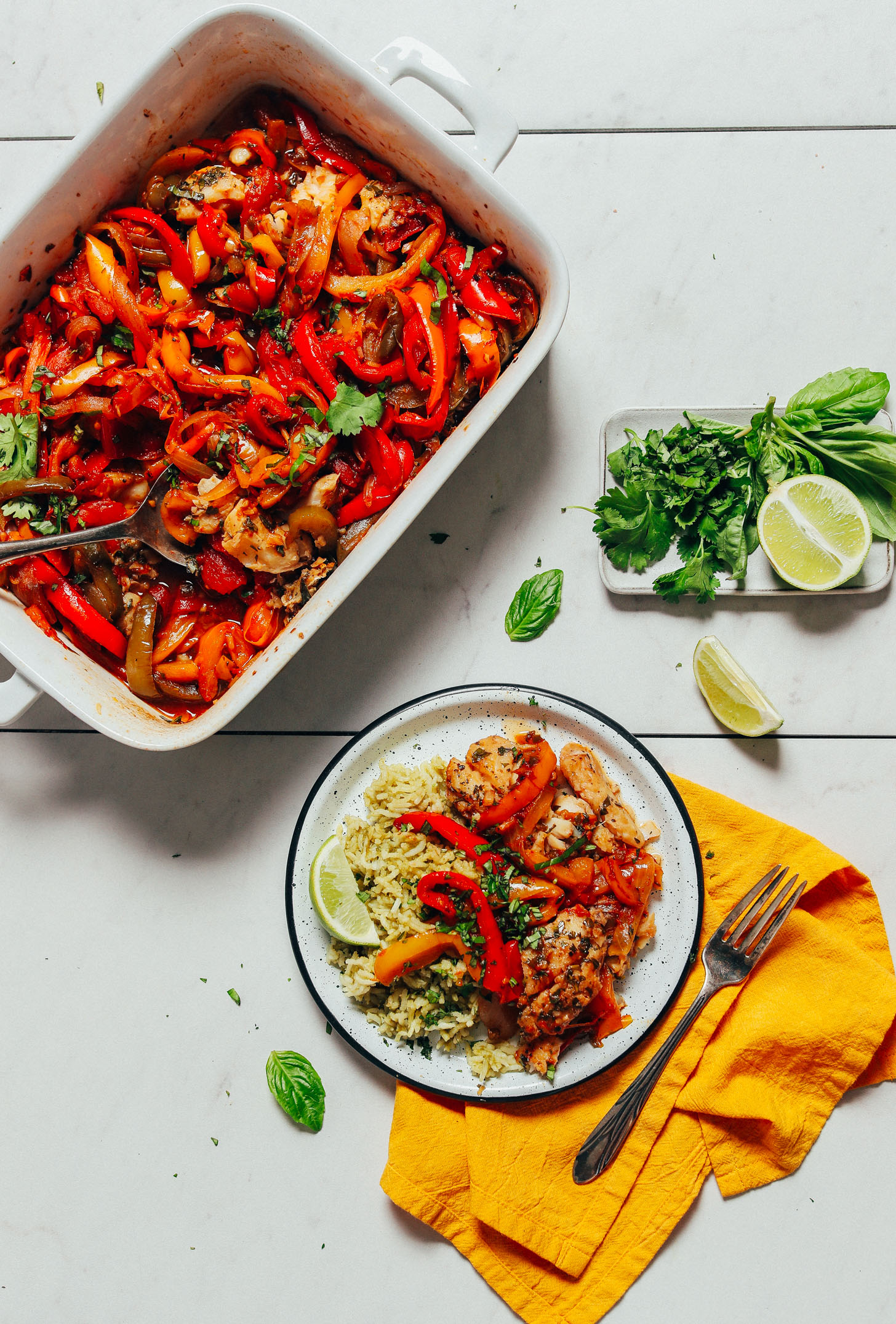 Plate of Herbed Green Rice topped with Baked White Fish with Rainbow Bell Peppers beside a baking pan with the remainder of the fish recipe