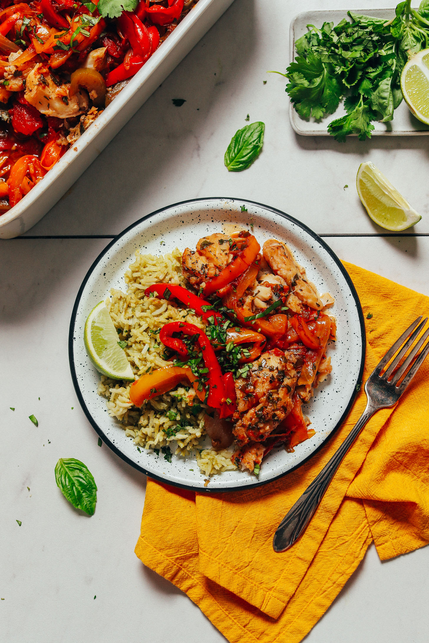 Plate of Baked White Fish with Rainbow Bell Peppers over green rice alongside fresh herbs and lime