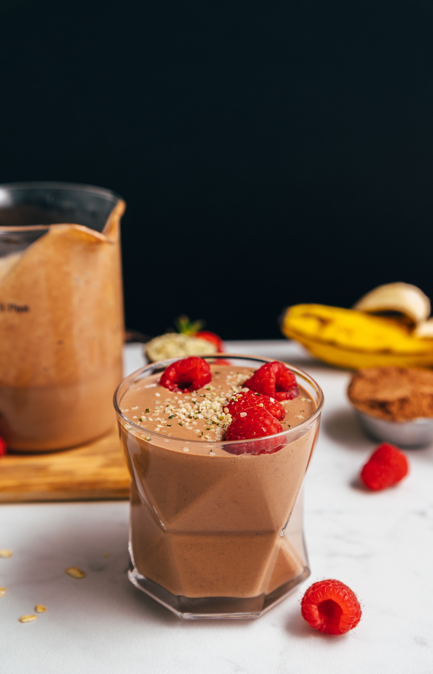 Glass of our Chocolate Protein Shake topped with fresh raspberries and hemp seeds