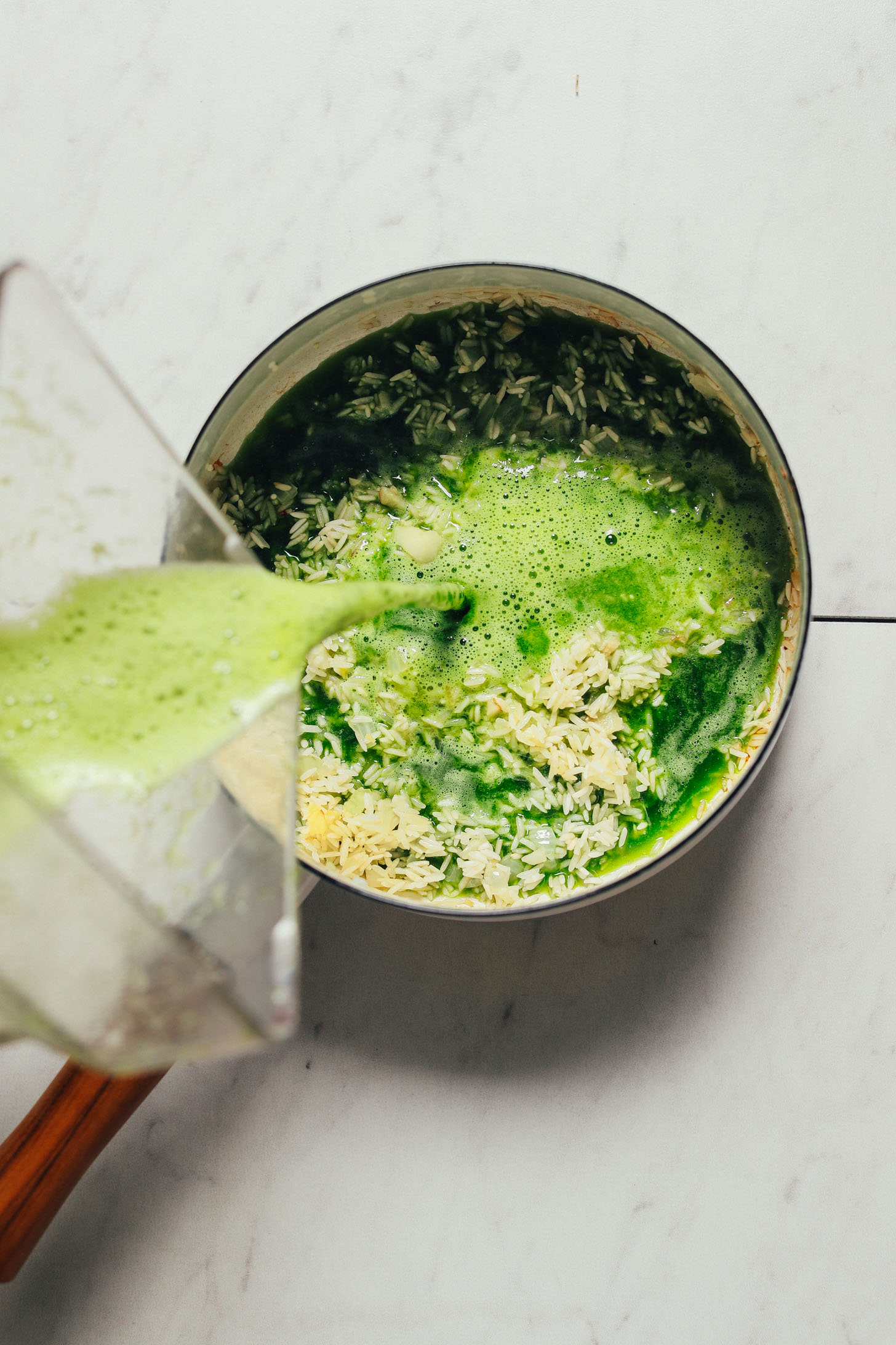 Pouring a green sauce made with cilantro, jalapeno, salt, and water into a pan of rice to make homemade Green Rice