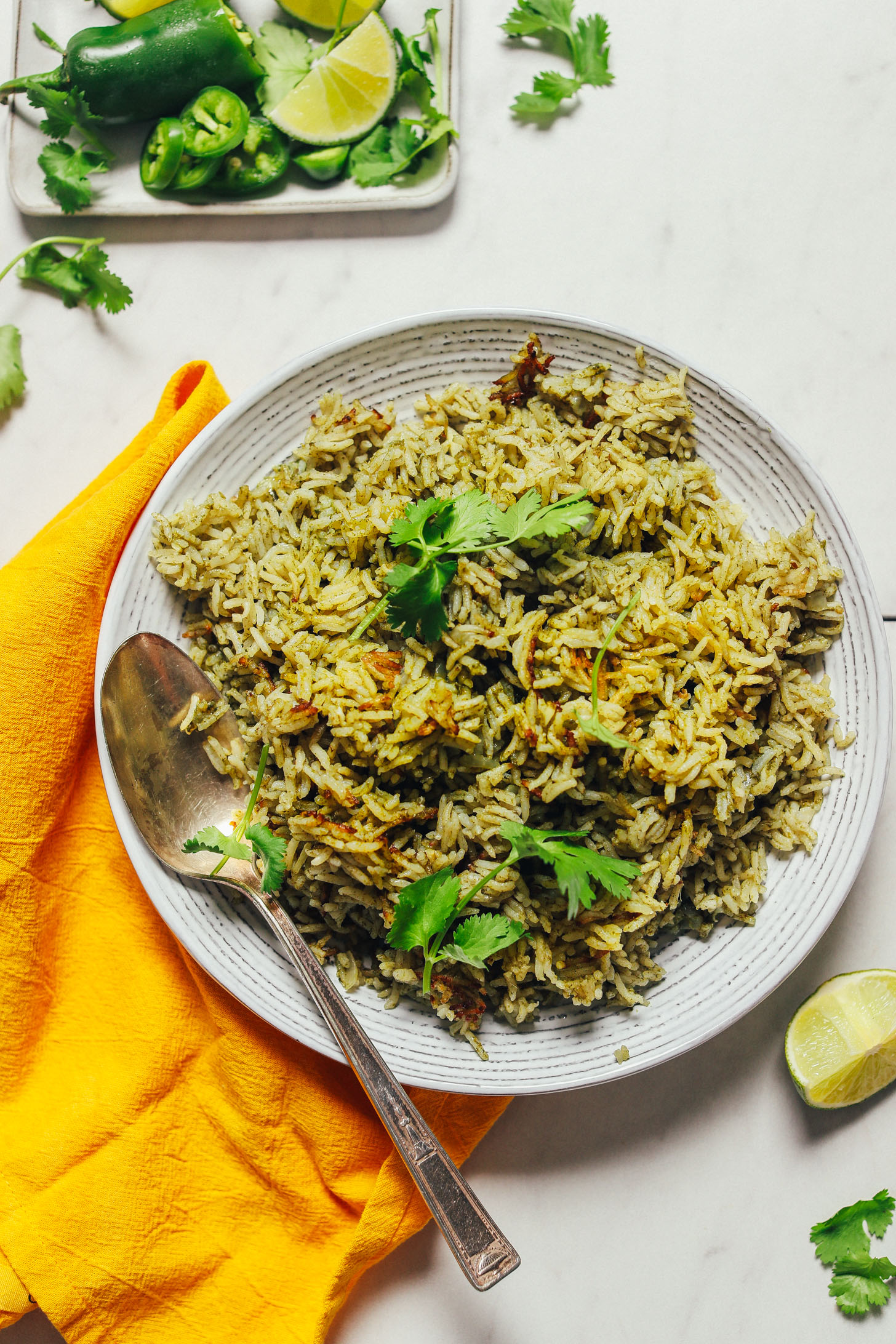 Bowl of homemade Green Rice beside a plate of jalapeno, lime, and cilantro used to make it
