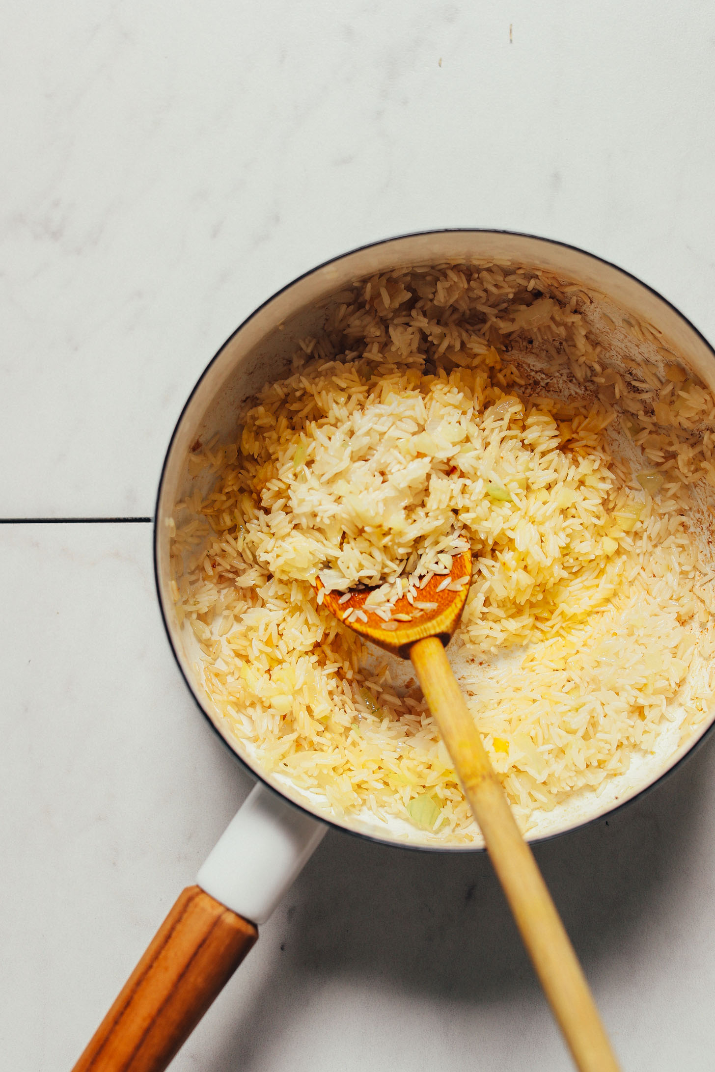 Using a wooden spoon to lightly toast rice in a skillet for our Mexican-inspired Green Rice recipe