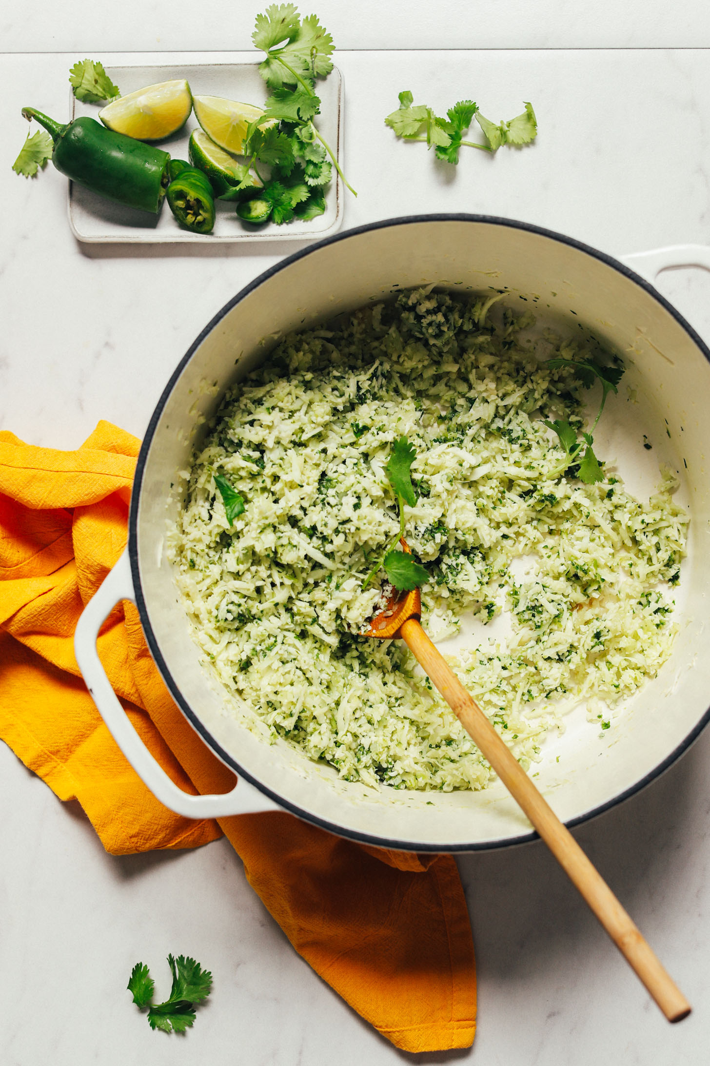 Using a wooden spoon to stir a pan of Cauliflower Green Rice made with lime, herbs, and peppers