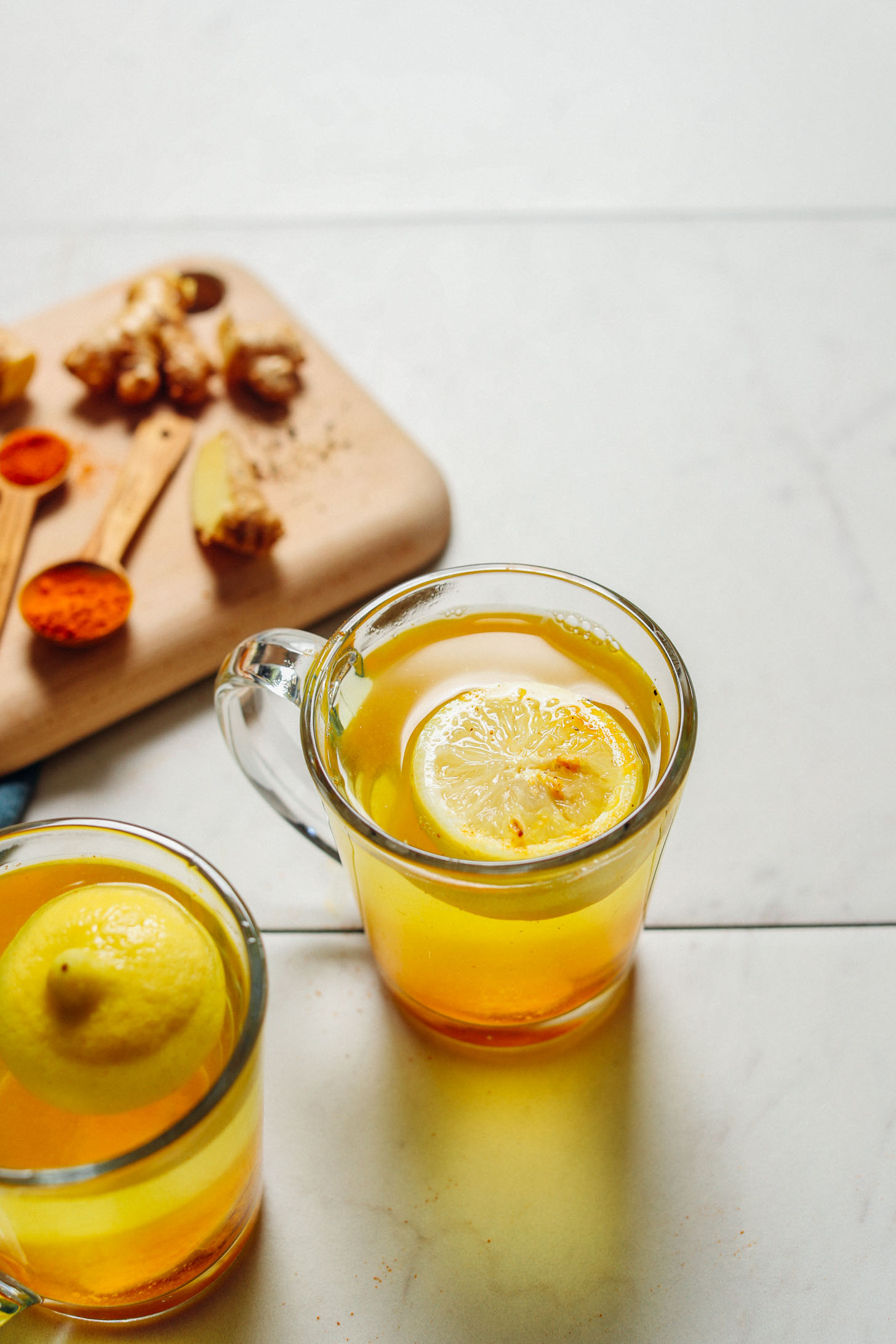 image of lemon ginger water in a mug with spoonfuls of turmeric and cayenne behind it
