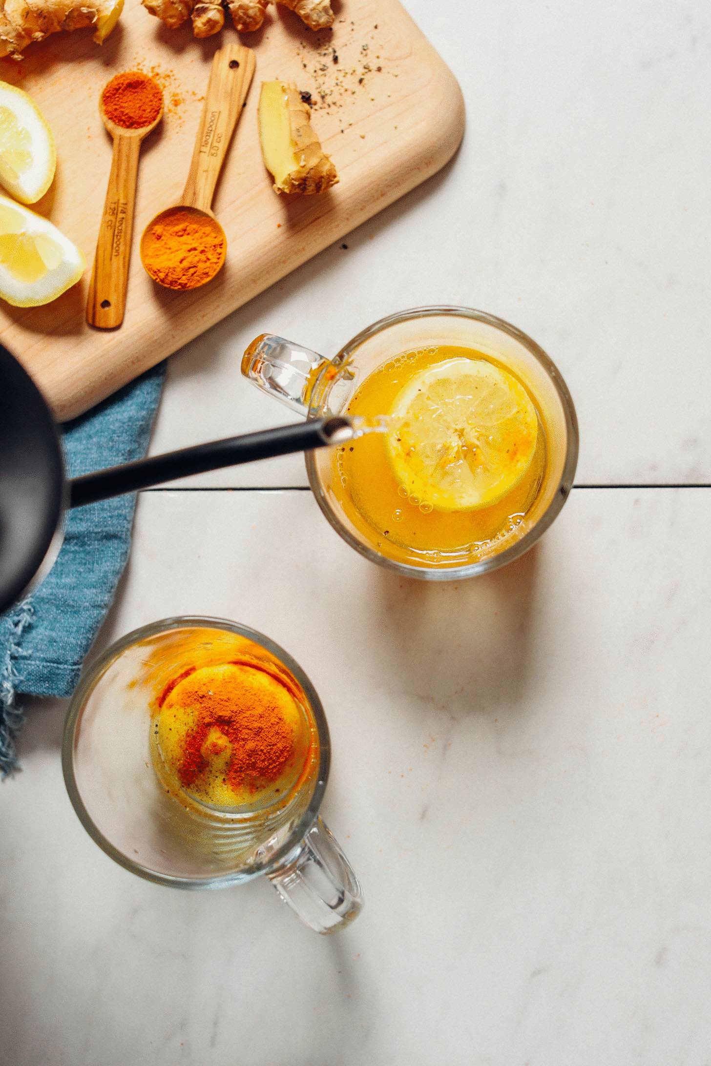 overhead image of lemon and ginger in mugs with hot water being poured on top