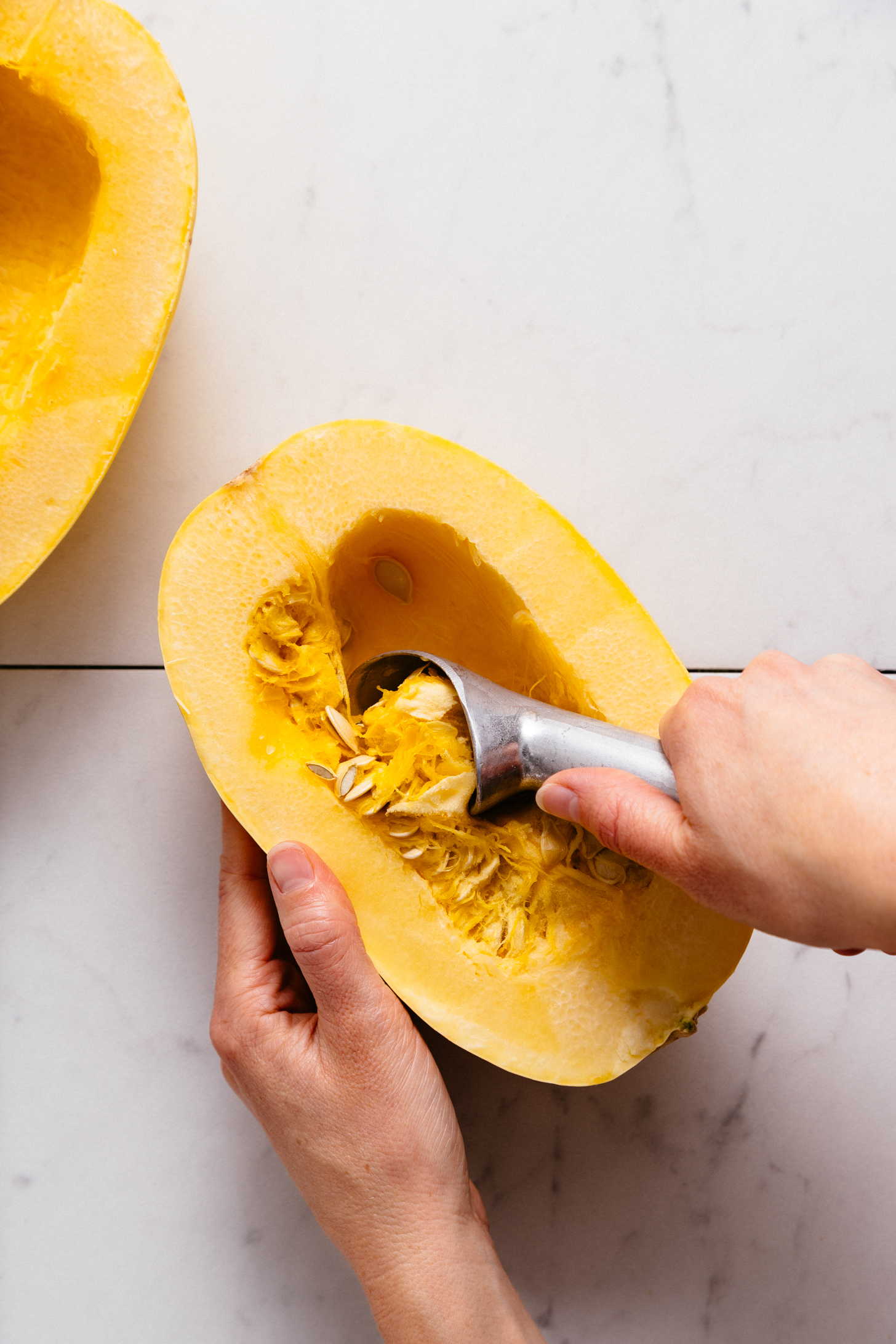 Using an ice cream scoop to remove seeds for our tutorial on How to Roast Spaghetti Squash
