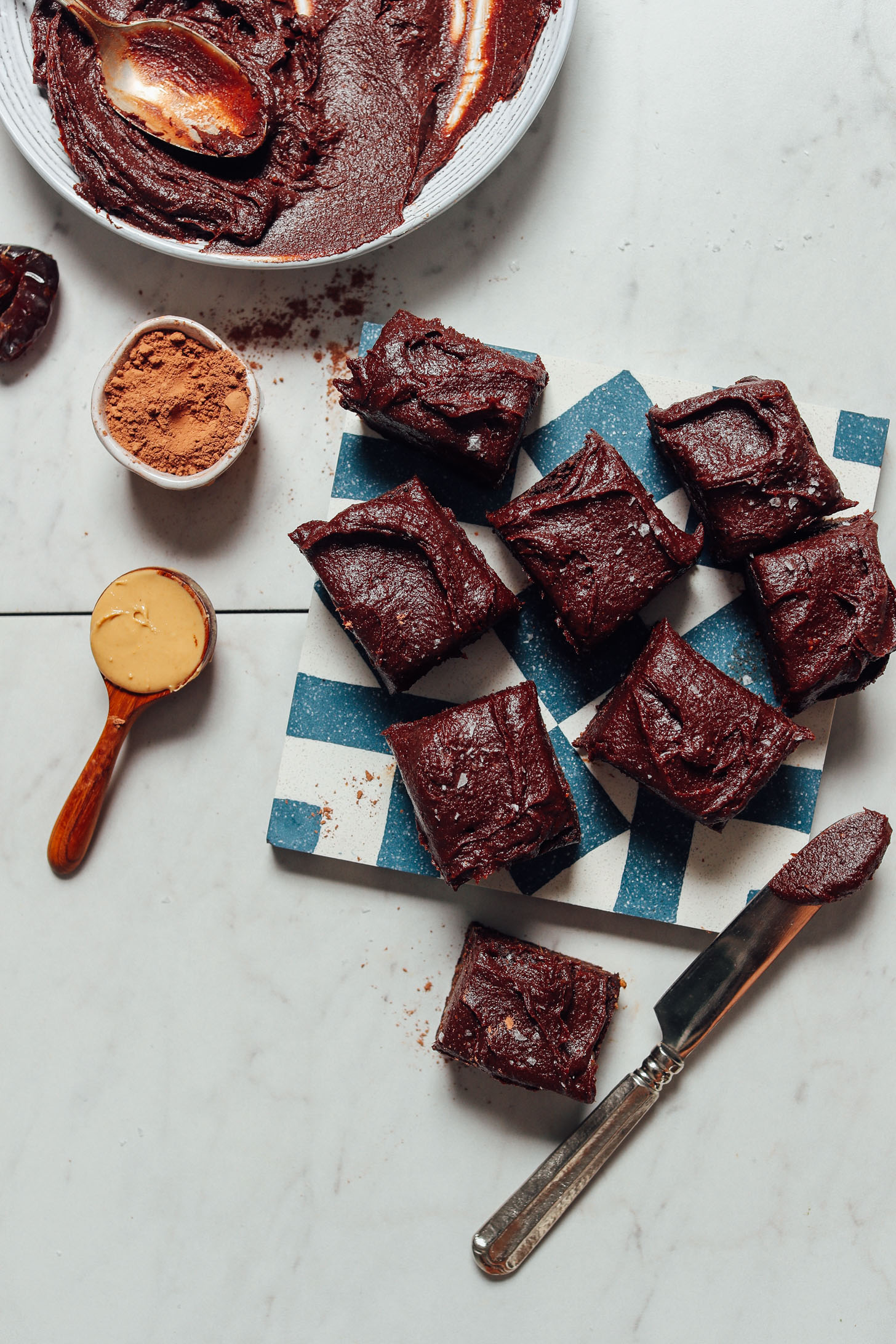 Brownies frosted with Vegan Chocolate Frosting beside the dates, cacao powder, and cashew butter used to make it