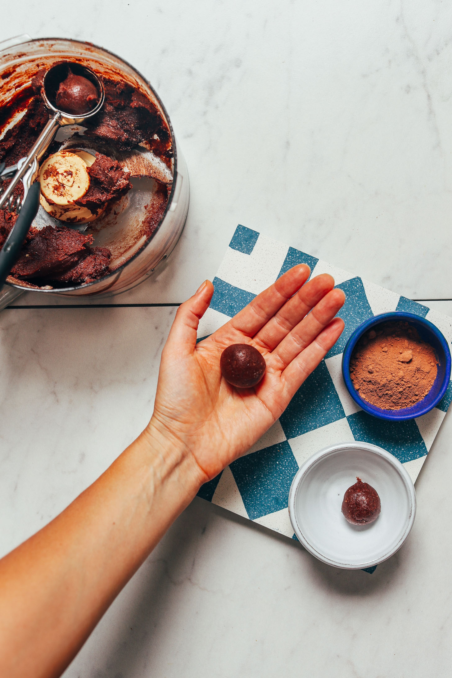 Holding a Vegan Chocolate Truffle next to a bowl of cocoa powder and more batter