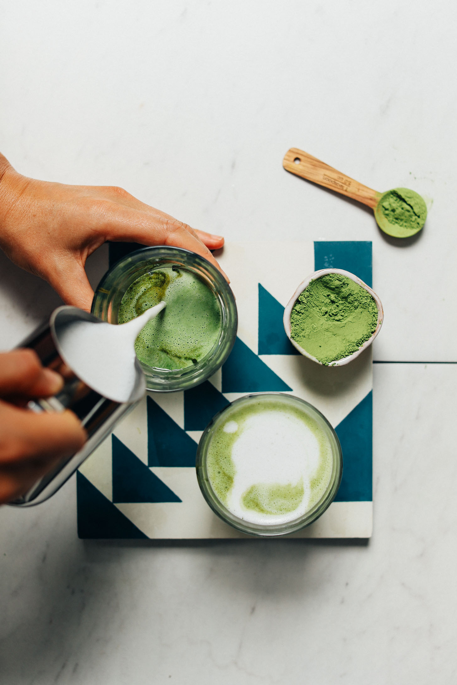 Pouring dairy-free steamed milk into a glass of moringa and water to make a Moringa Latte