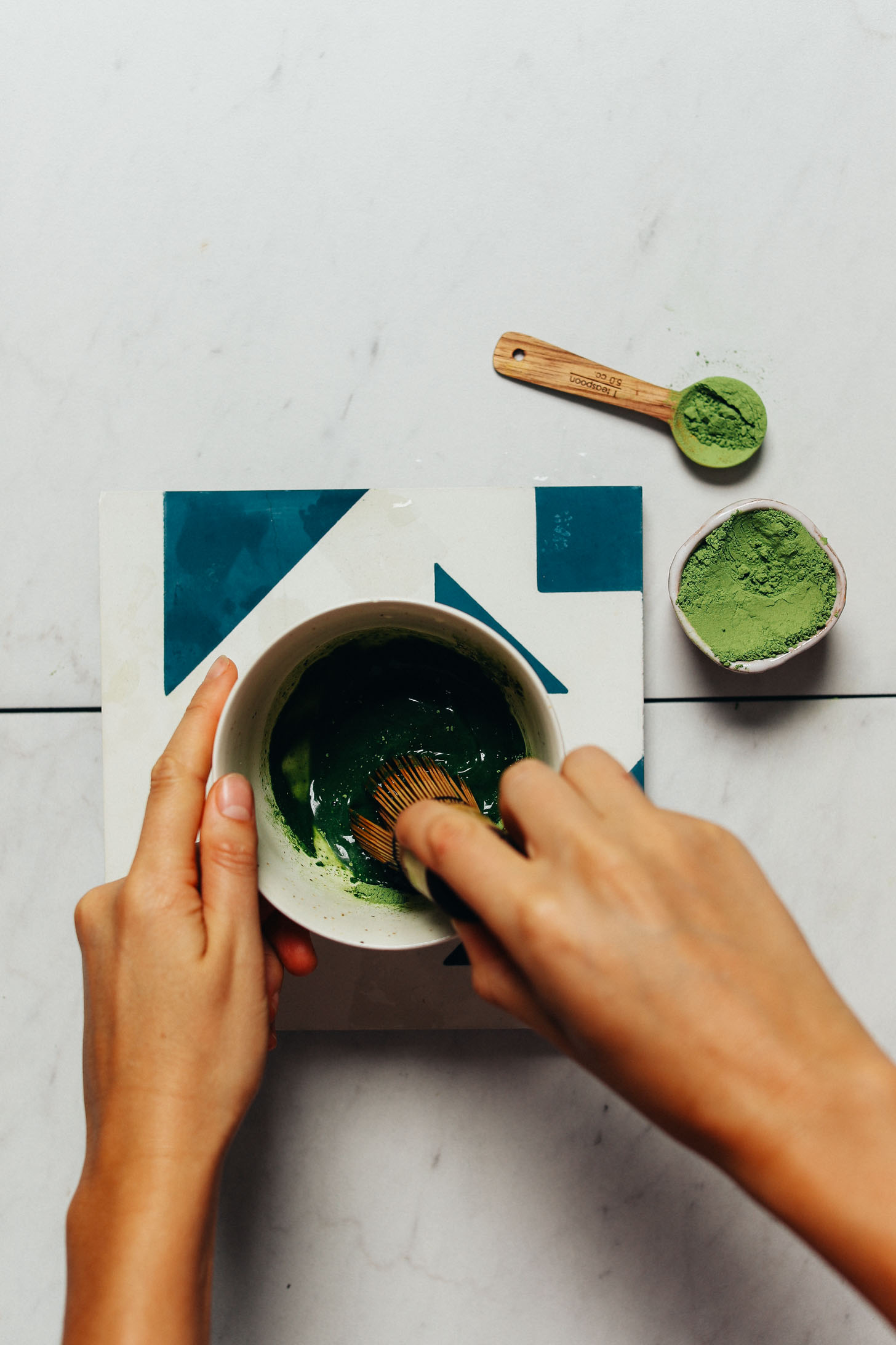 Using a bamboo whisk to mix moringa powder into water for a homemade Moringa Latte