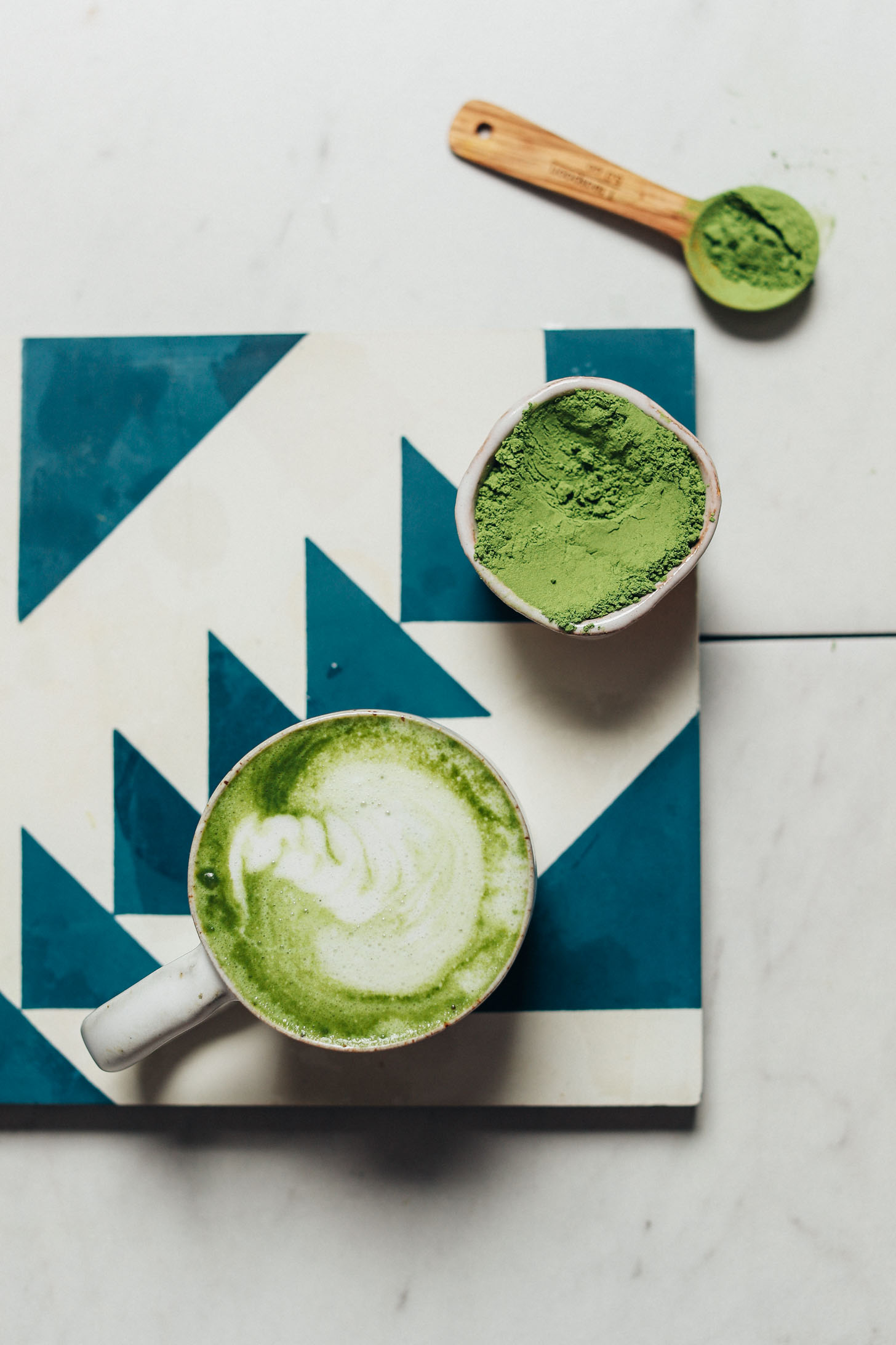 Tile with a ceramic dish of moringa powder and mug of our Moringa Latte recipe