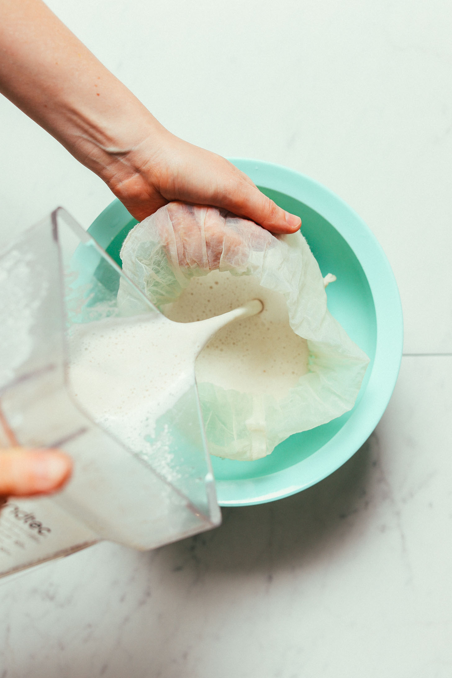 Pouring homemade creamy Cashew Coconut Oat Milk through a nut milk bag