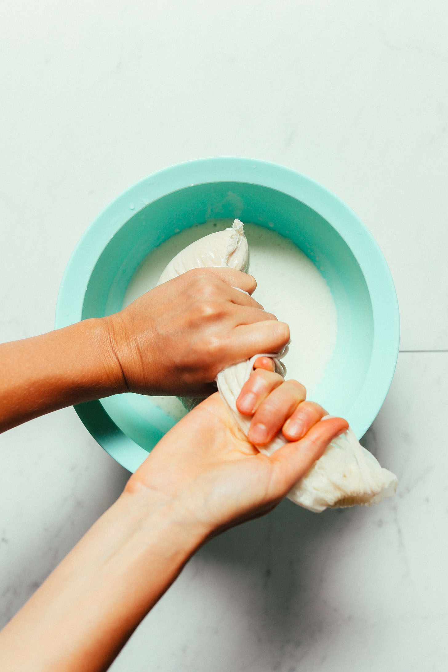 Using a nut milk bag to strain homemade Cashew Coconut Oat Milk into a large bowl