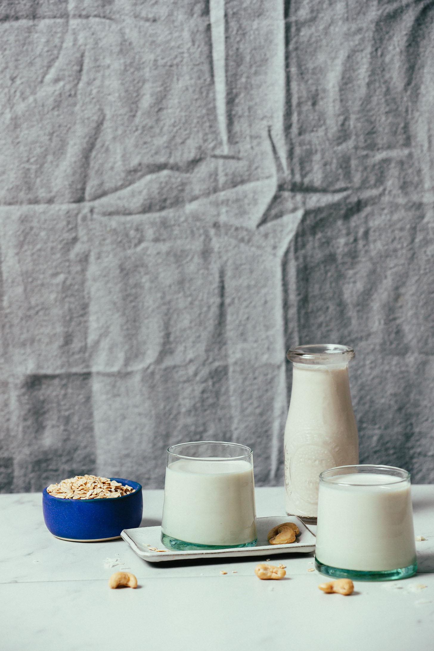 Glasses of homemade Cashew Oat Coconut Milk Creamer surrounded by ingredients use to make it
