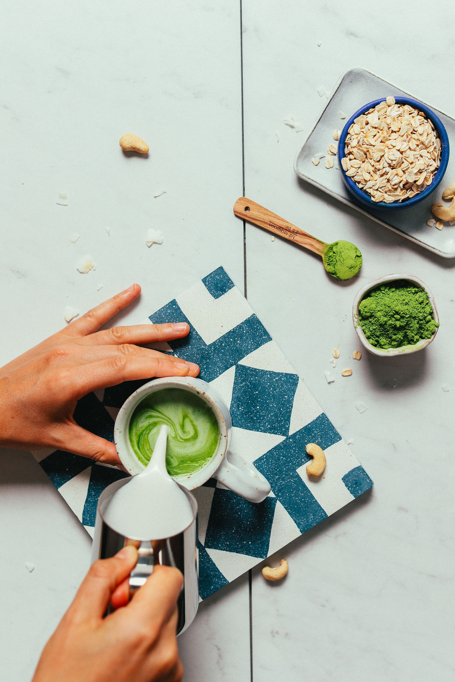 Pouring homemade creamy oat milk into a mug of matcha