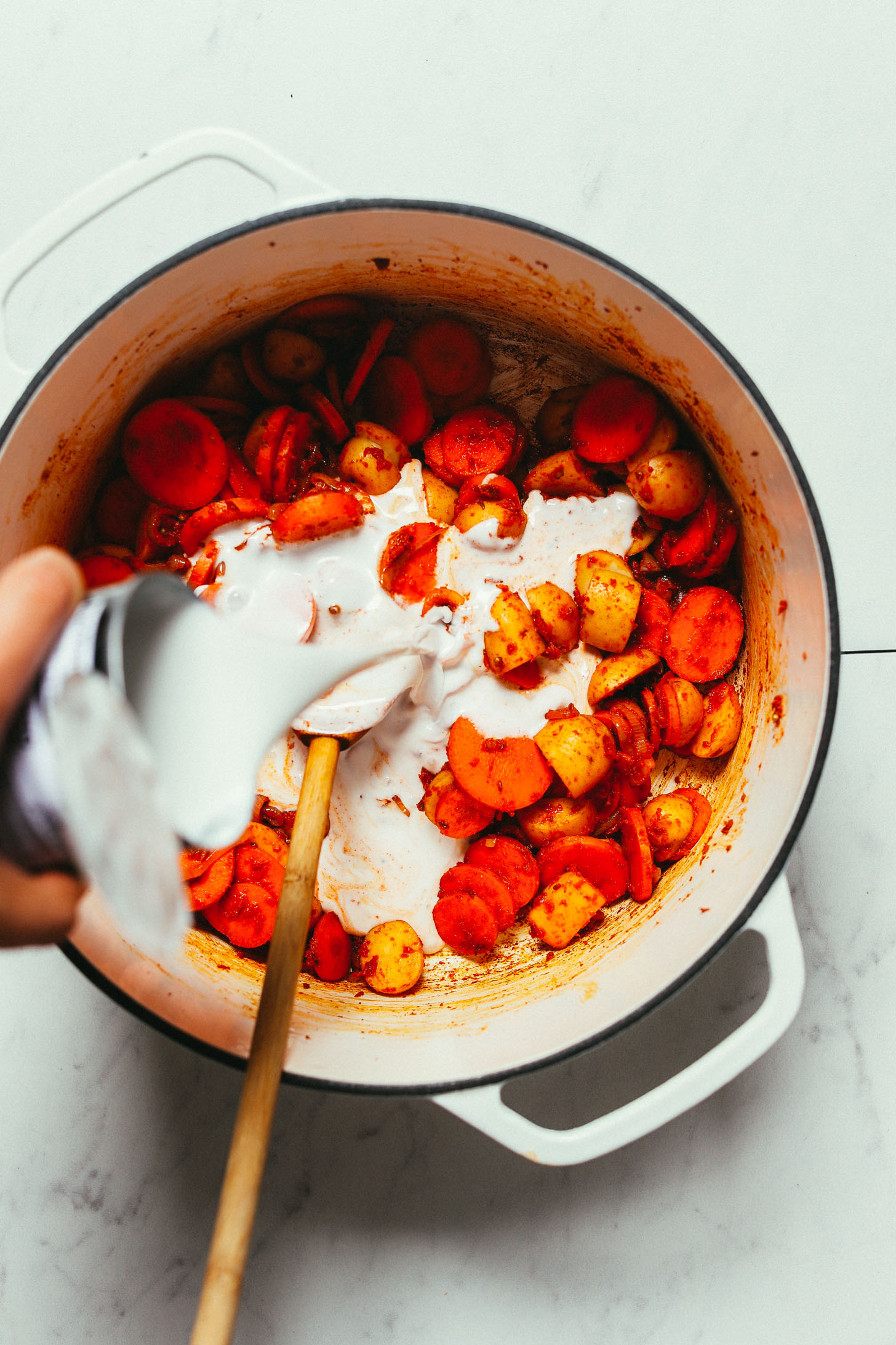 Pouring coconut milk into a pot of vegan Massaman Curry