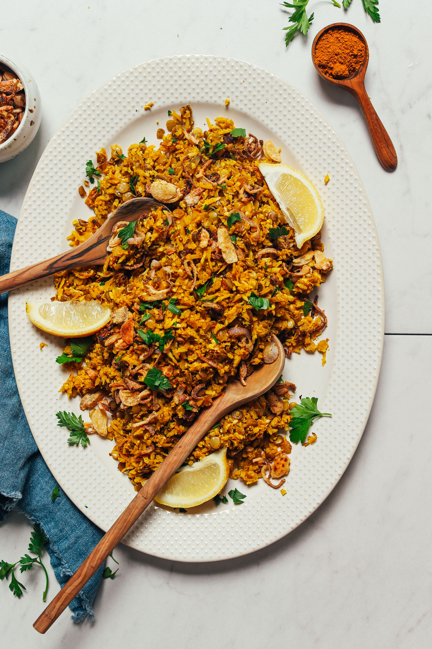 Wooden serving spoons on a large platter of homemade Mujadara with fresh lemon wedges and parsley