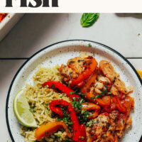 Plate of rice toped with herb baked fish and rainbow bell peppers