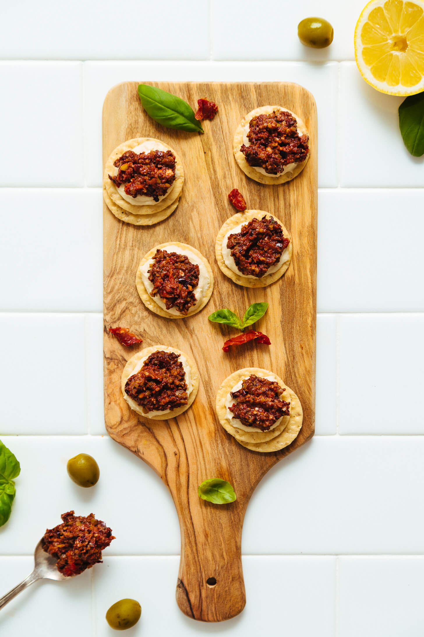 Wood cutting board filled with rice crackers, hummus, and homemade Sun-Dried Tomato and Basil Olive Tapenade