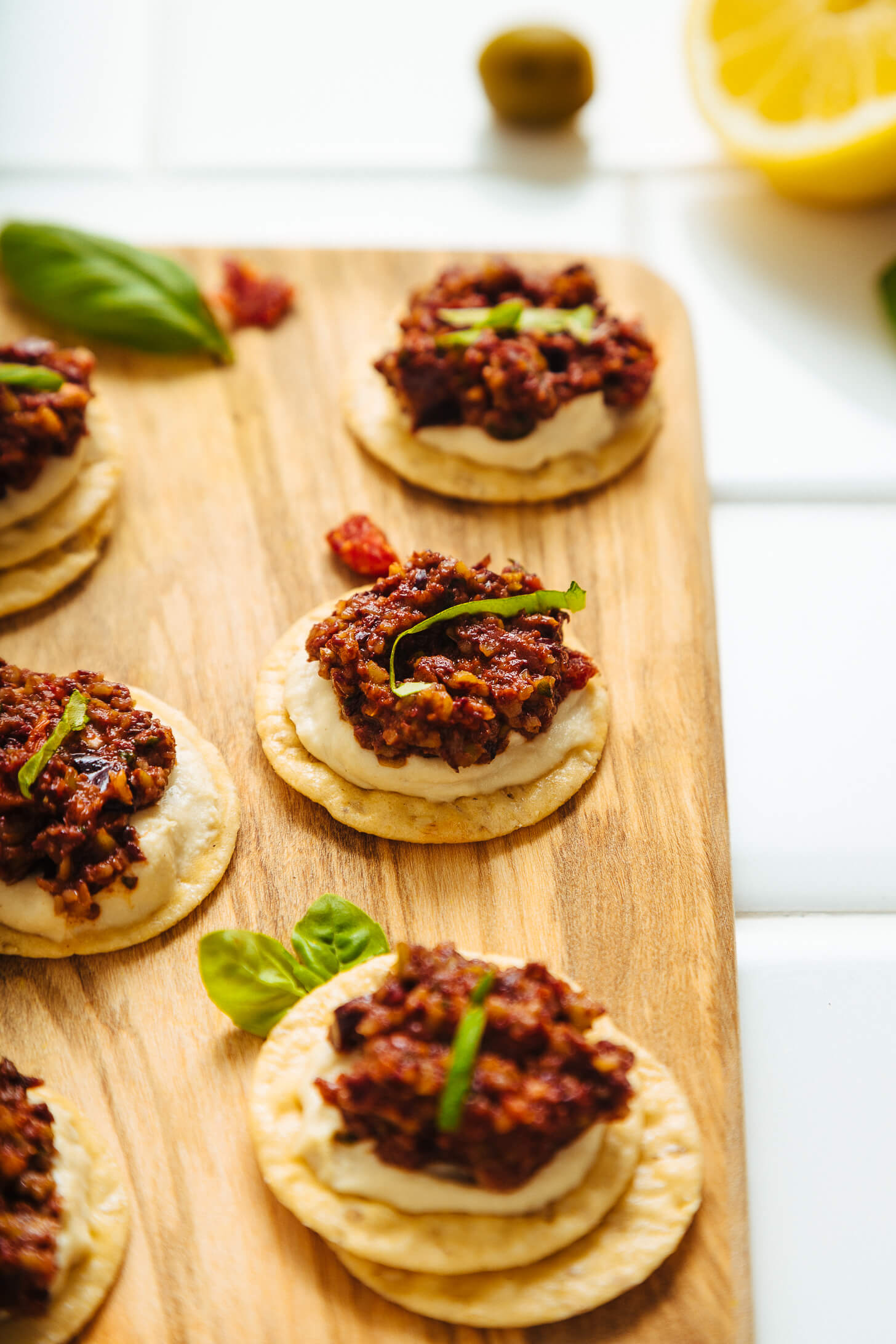 Cutting board of crackers topped with hummus and homemade Sun-Dried Tomato and Basil Olive Tapenade