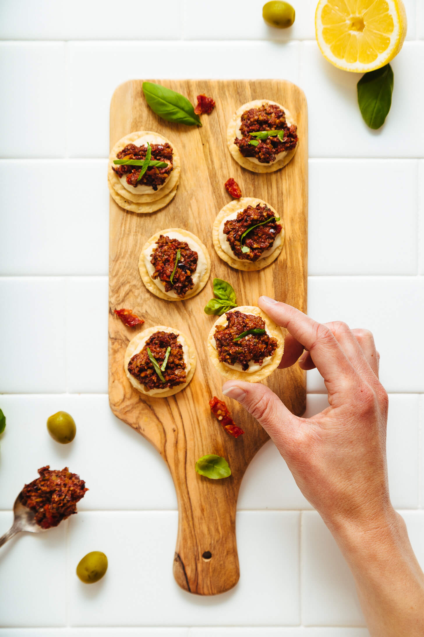 Picking up a cracker topped with Sun-Dried Tomato and Basil Tapenade for a delicious vegan appetizer