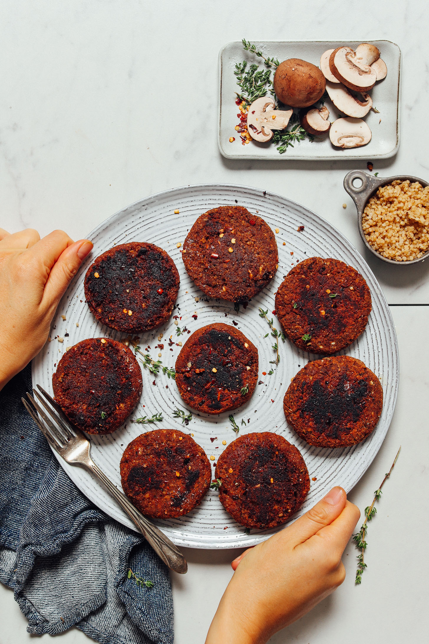 Holding a platter of Easy Vegan Sausage patties beside quinoa, mushrooms, and fresh thyme