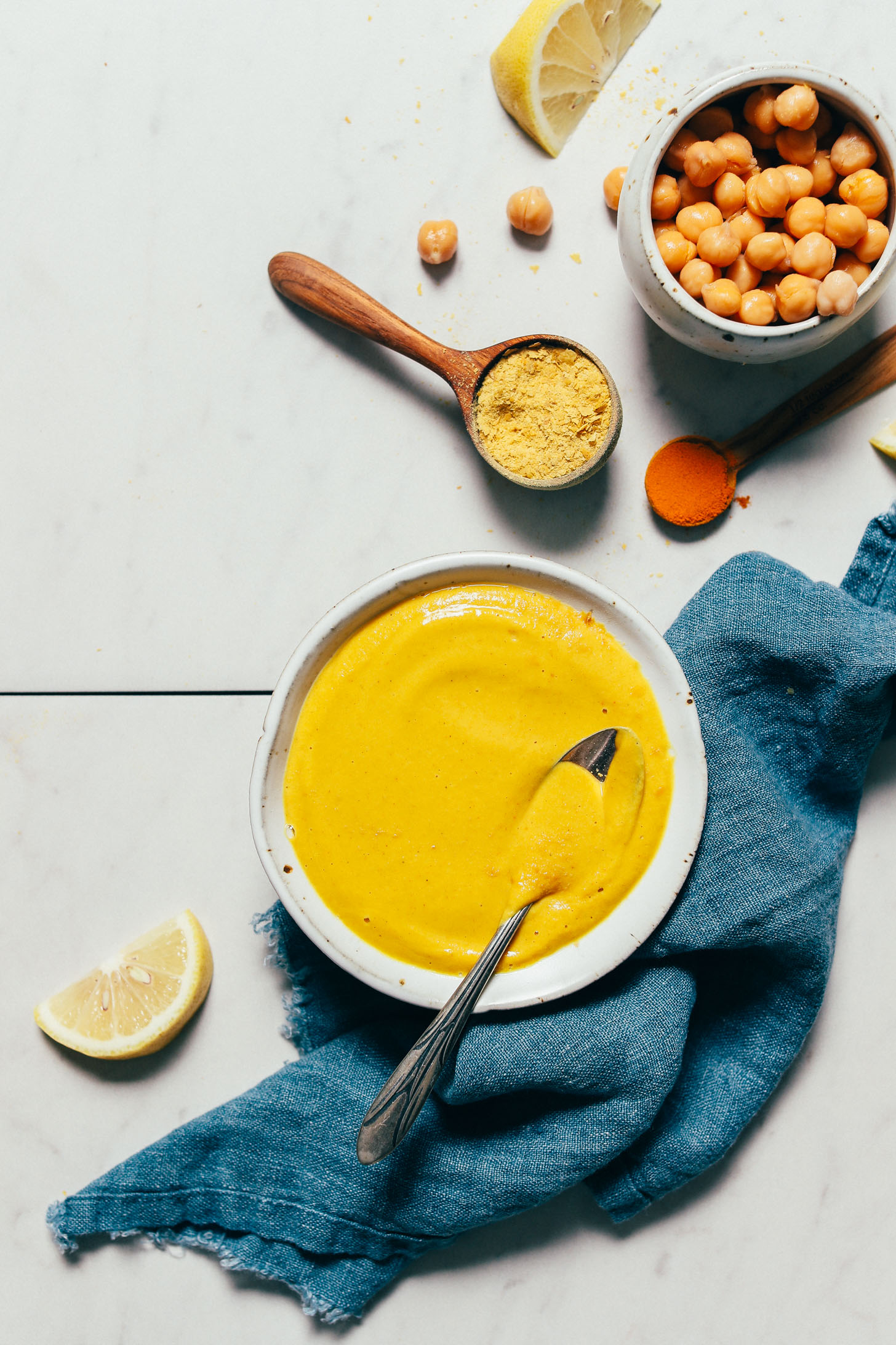 Bowl of Liquid Gold Chickpea Sauce beside spoonfuls of turmeric and nutritional yeast