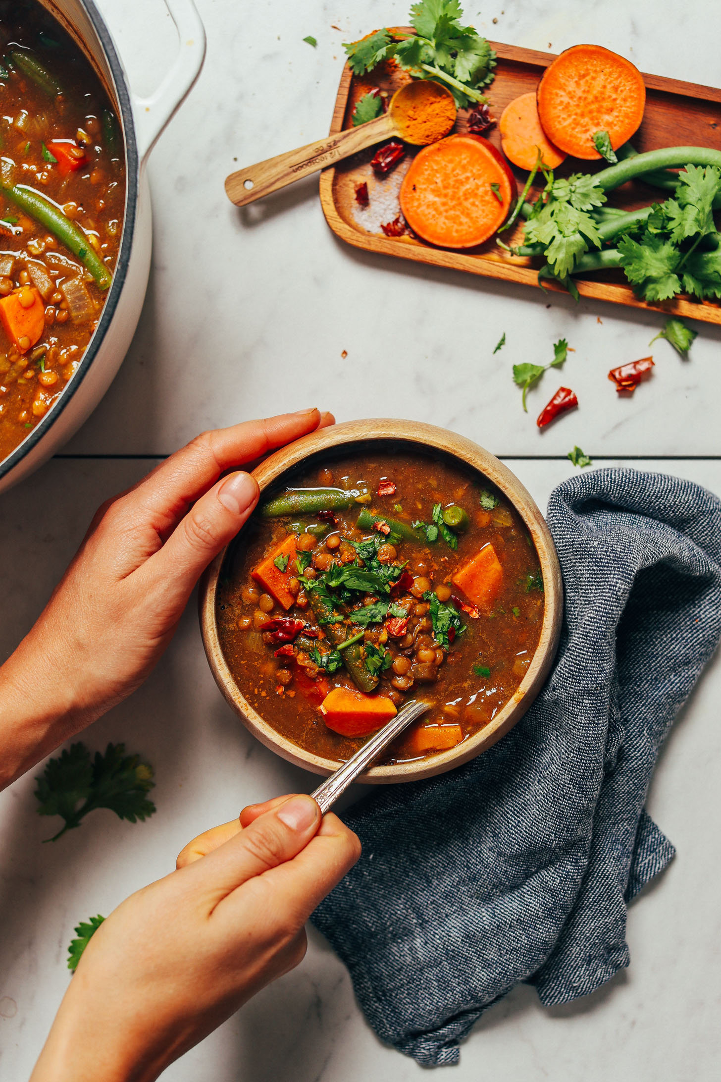 Bowl and pot of Spiced Sweet Potato Lentil Soup beside ingredients used to make it