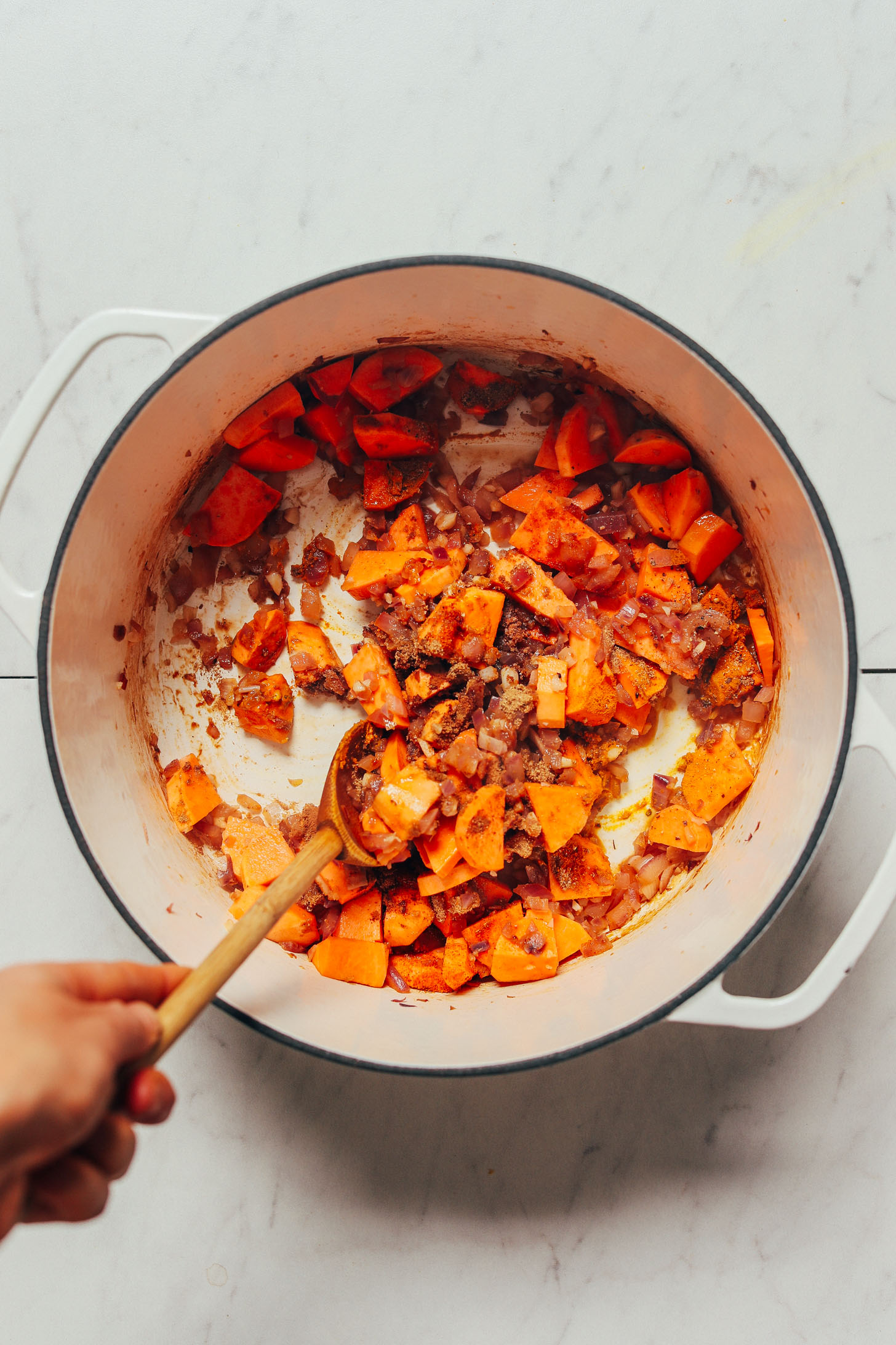 Using a wooden spoon to stir sweet potato and other ingredients for making our Spiced Lentil Soup recipe