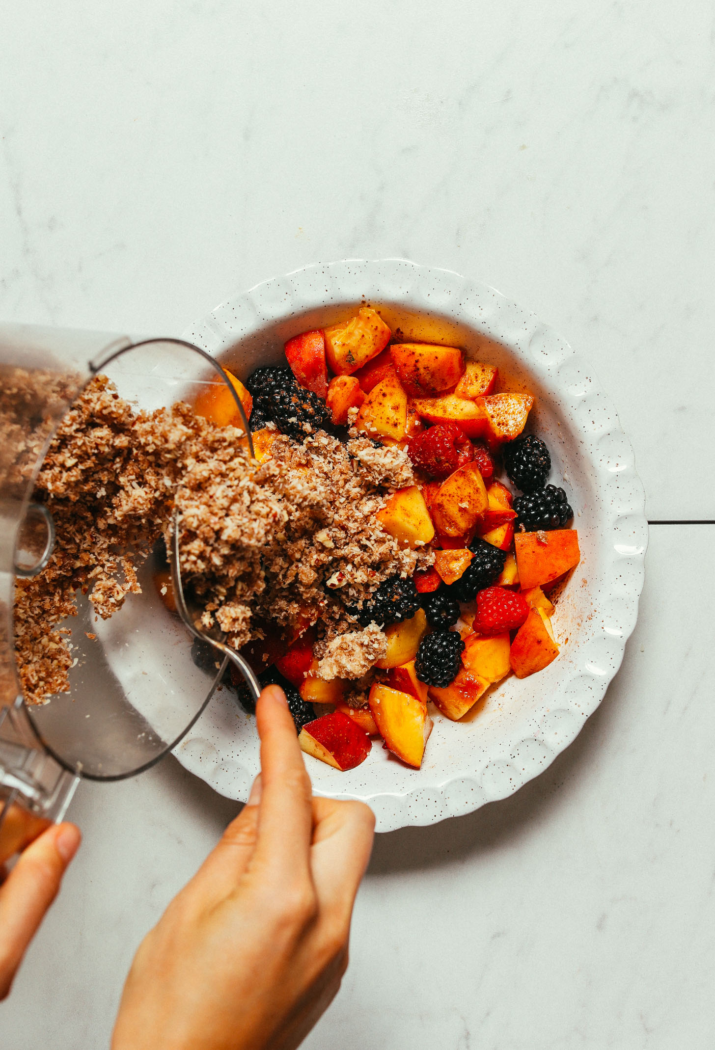 Pouring date-sweetened crisp topping onto fresh fruit for an easy Fruit Crisp recipe