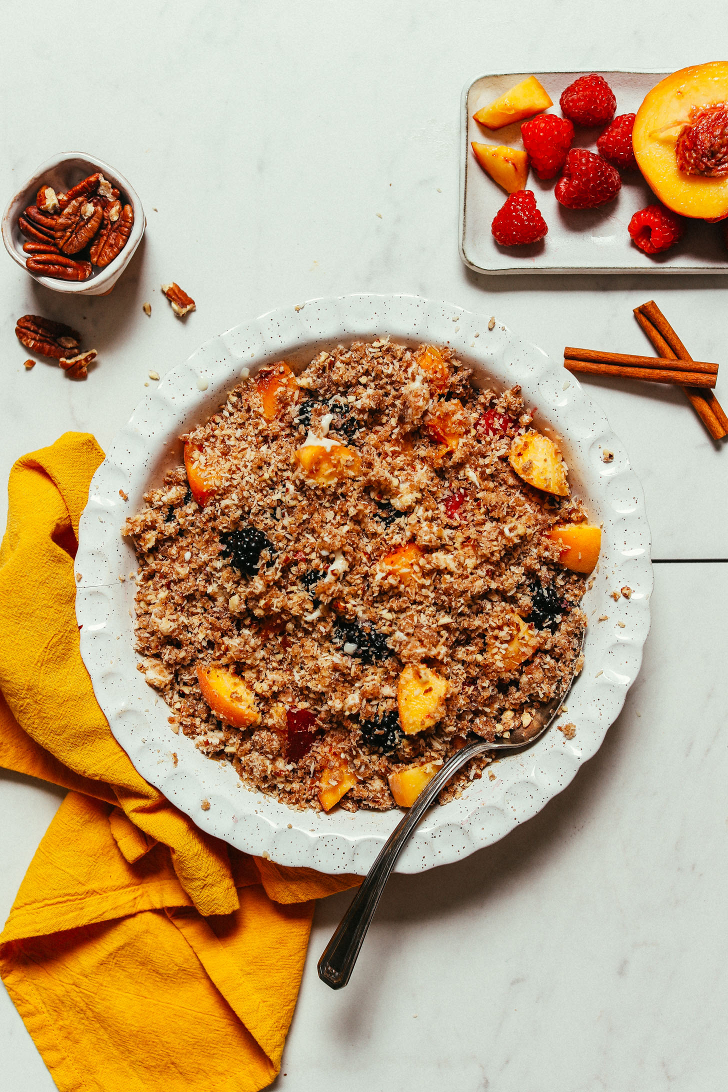 Pie pan of our Gluten-Free Fruit Crisp recipe beside pecans, cinnamon, and fruit used to make it
