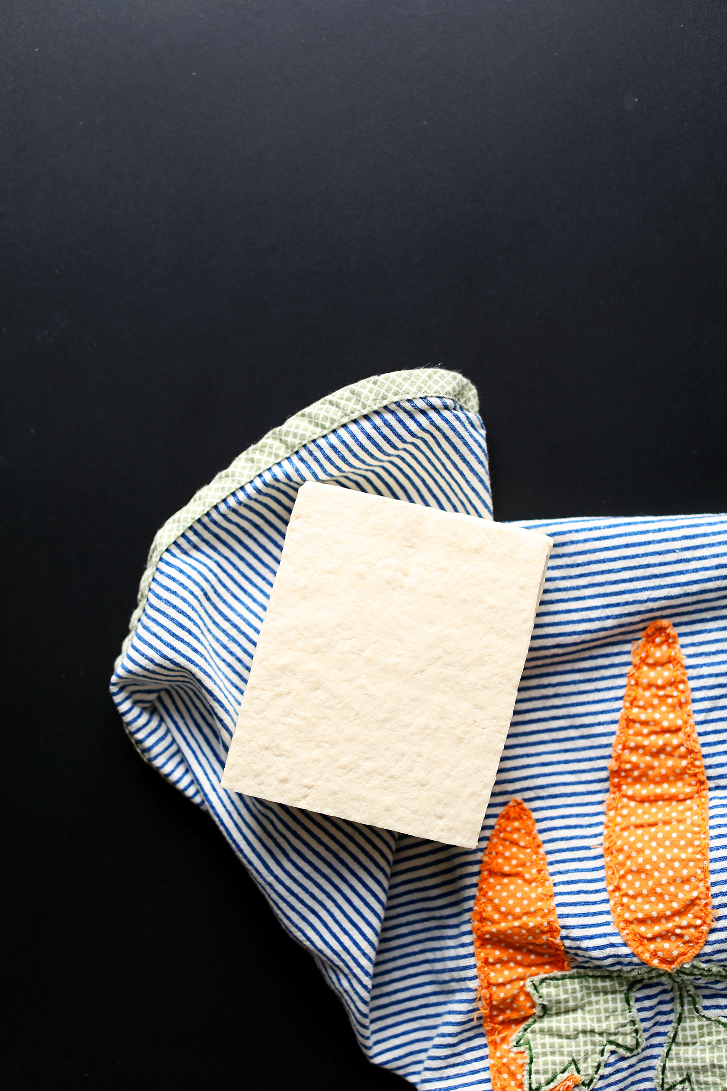 overhead image of a block of tofu being dried on a blue striped towel
