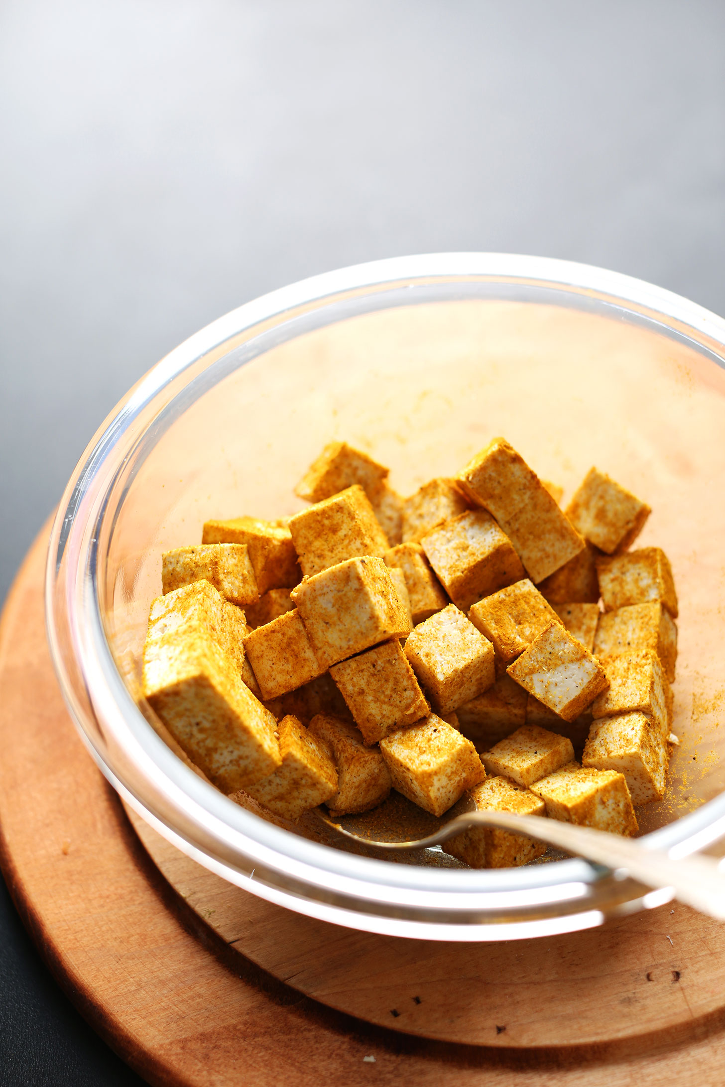 Cubed tofu tossed in curry powder in a glass mixing bowl