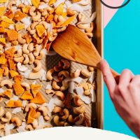Using a wooden spatula to stir a batch of homemade Trail Mix made with mango, coconut, and cashews