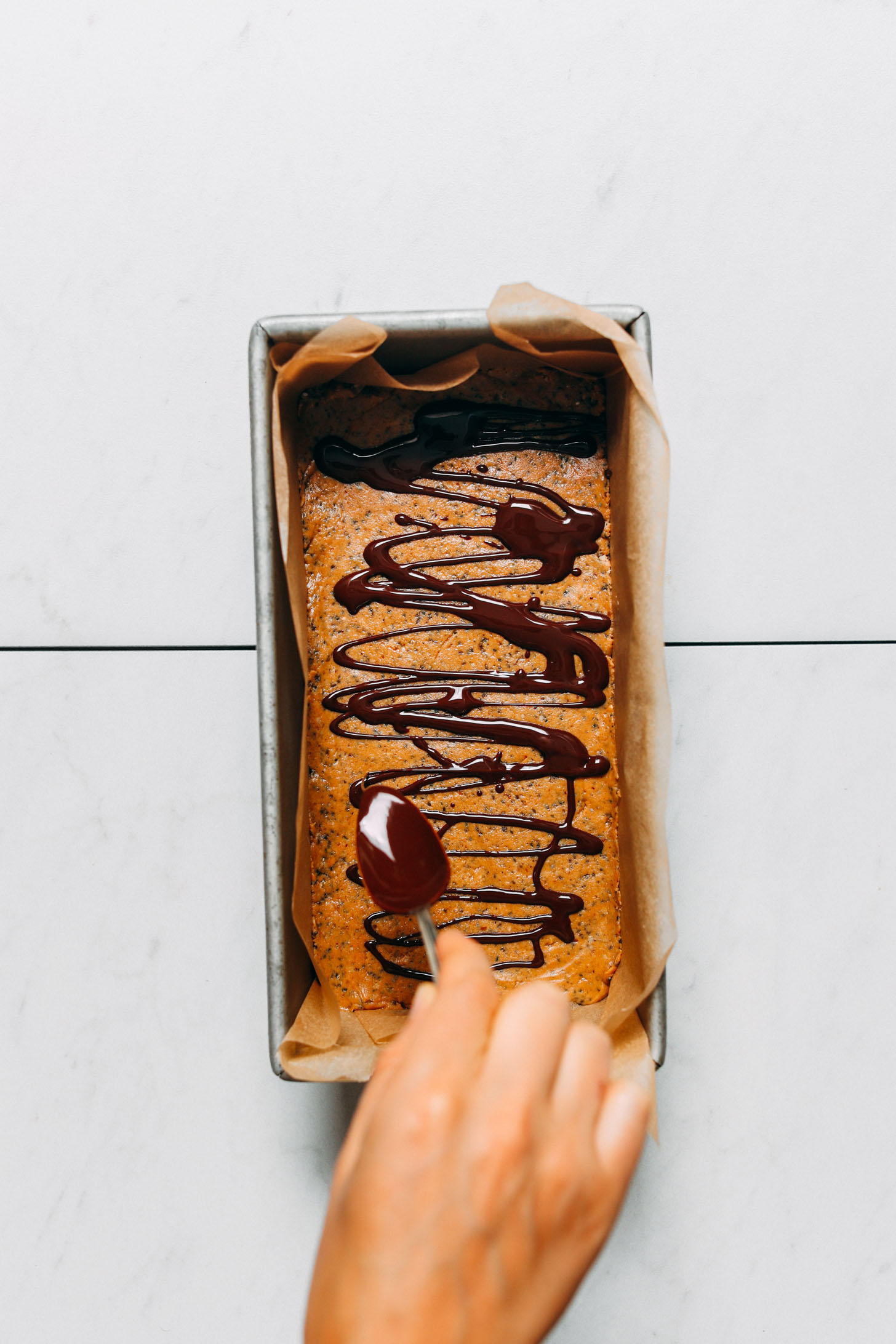 Drizzling melted dark chocolate onto a batch of homemade peanut butter protein bars