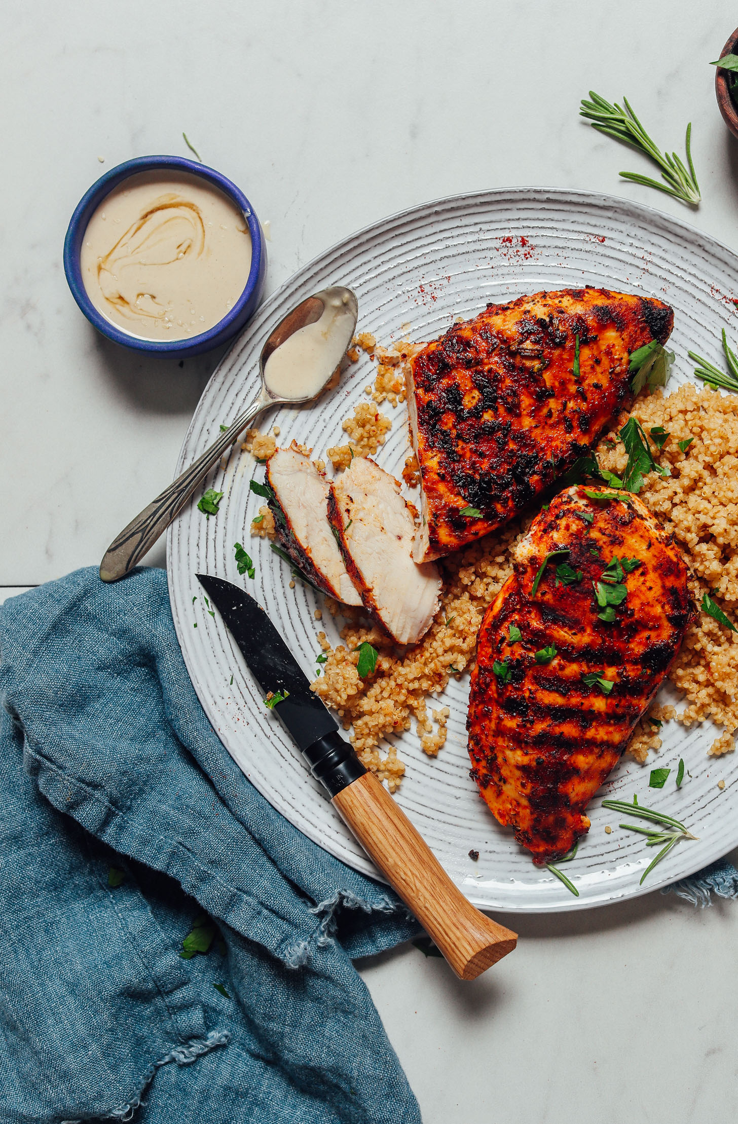 Bowl of tahini sauce beside a plate of Marinated Grilled Chicken Breasts served over quinoa