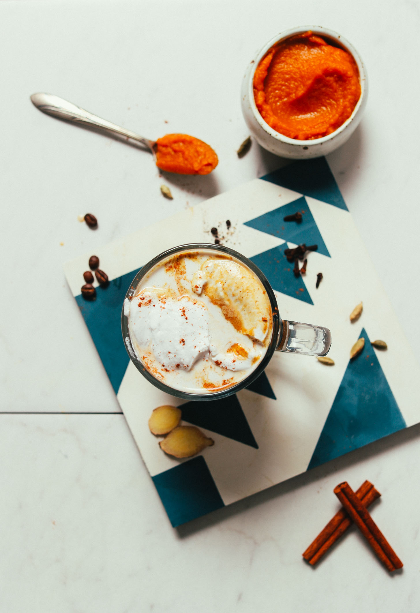 Mug of our homemade Pumpkin Spice Latte beside pumpkin puree and spices