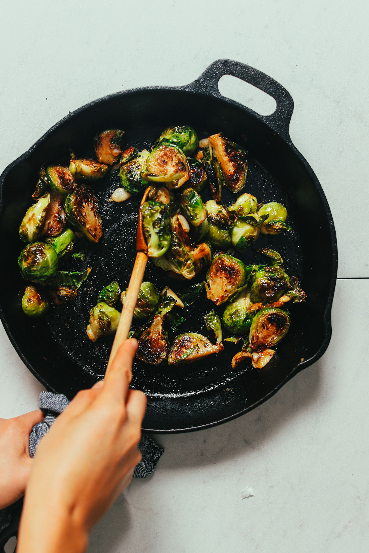 Using a wooden spoon to coat Roasted Brussels Sprouts with Miso Glaze for a delicious Thanksgiving side