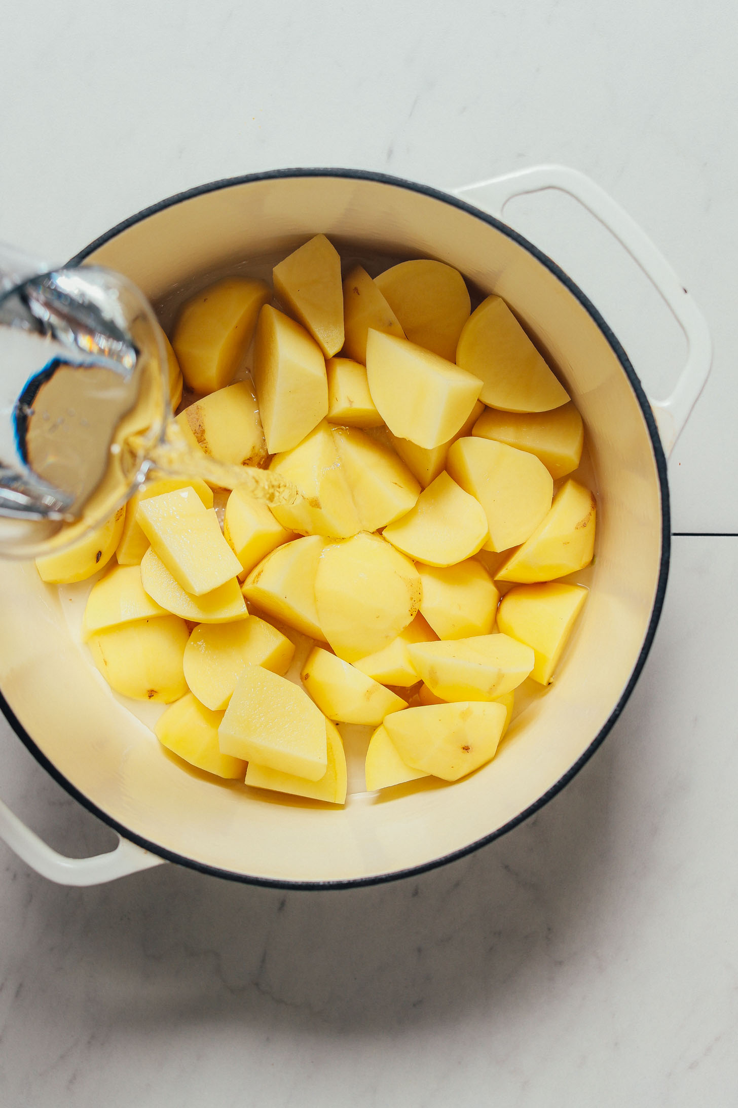 Pouring water into a pot of gold potatoes to make our homemade Mashed Potatoes recipe