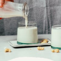 Pouring a glass of Creamy Cashew Coconut Oat Milk for our copycat Oatly creamer recipe