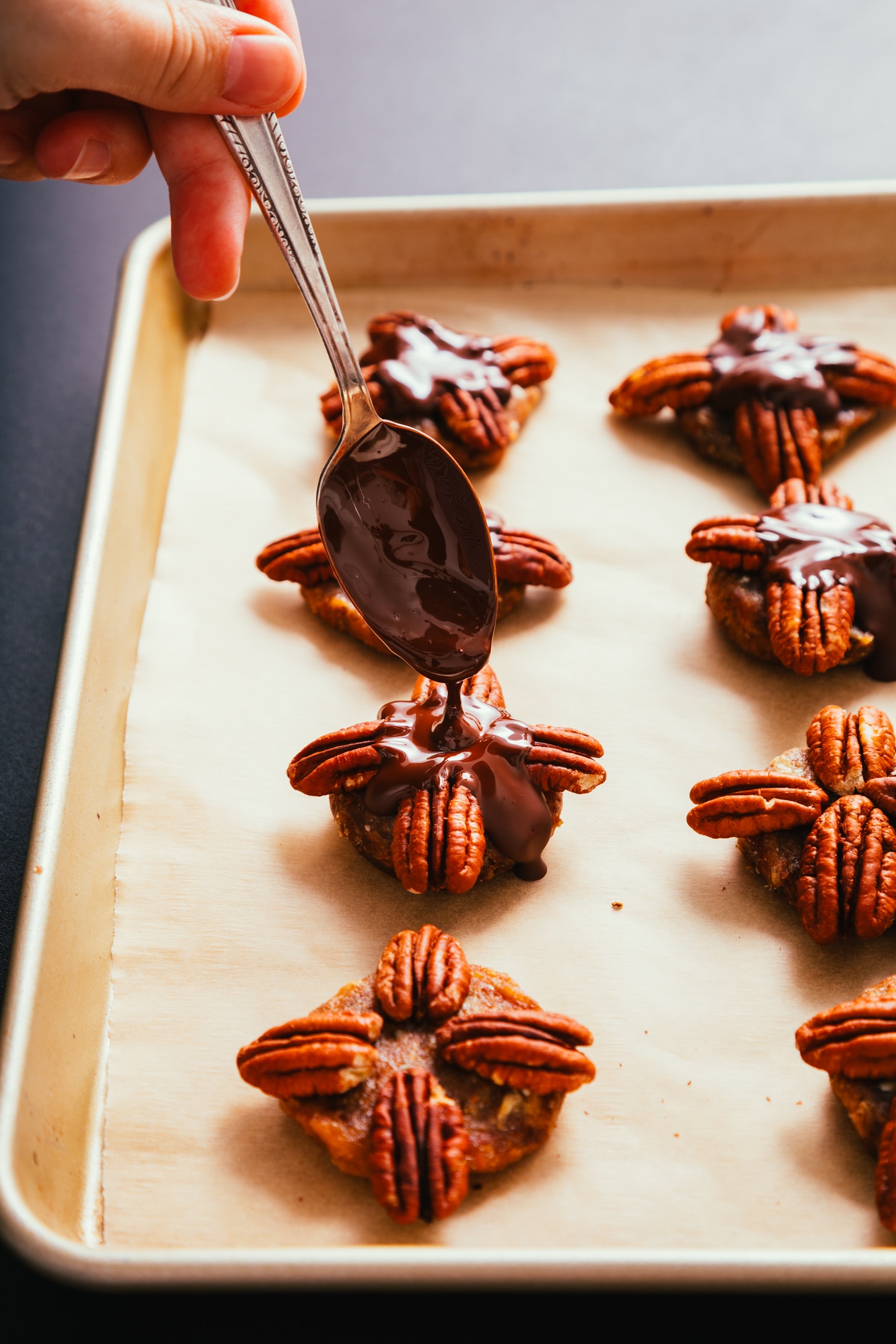 Drizzling melted chocolate onto Vegan Chocolate Turtles made with pecans and dates